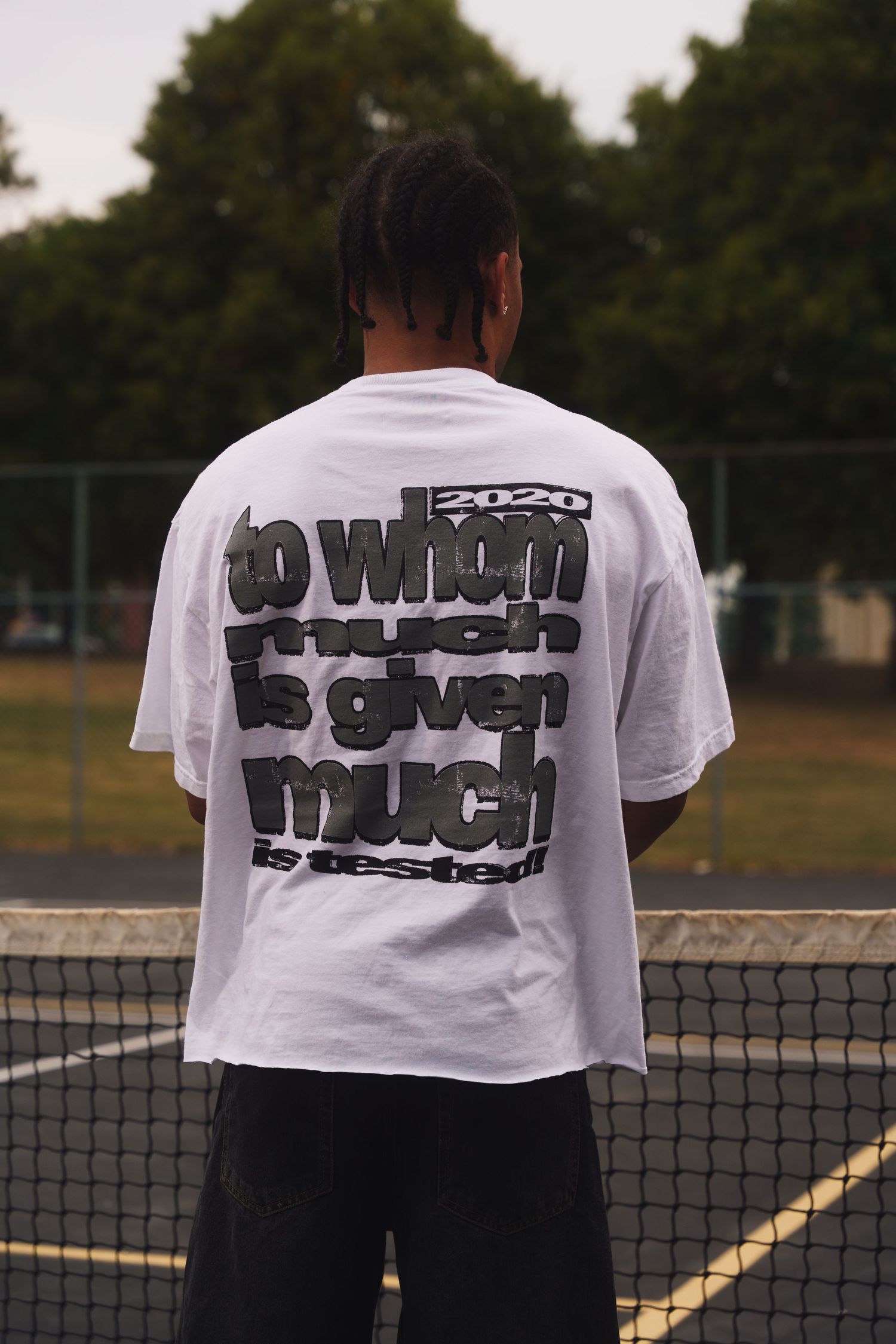 White t-shirt with graphic text design shown from behind on tennis court.