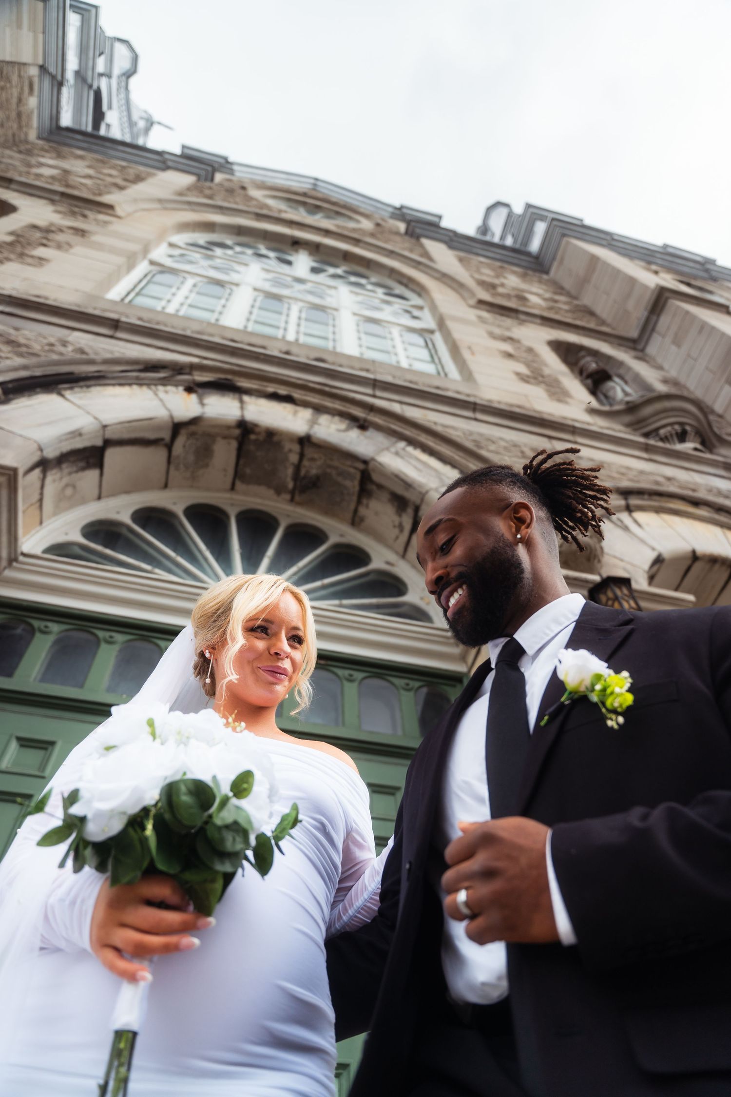A happy couple celebrates their wedding day outside a historic building with ornate architectural details.
