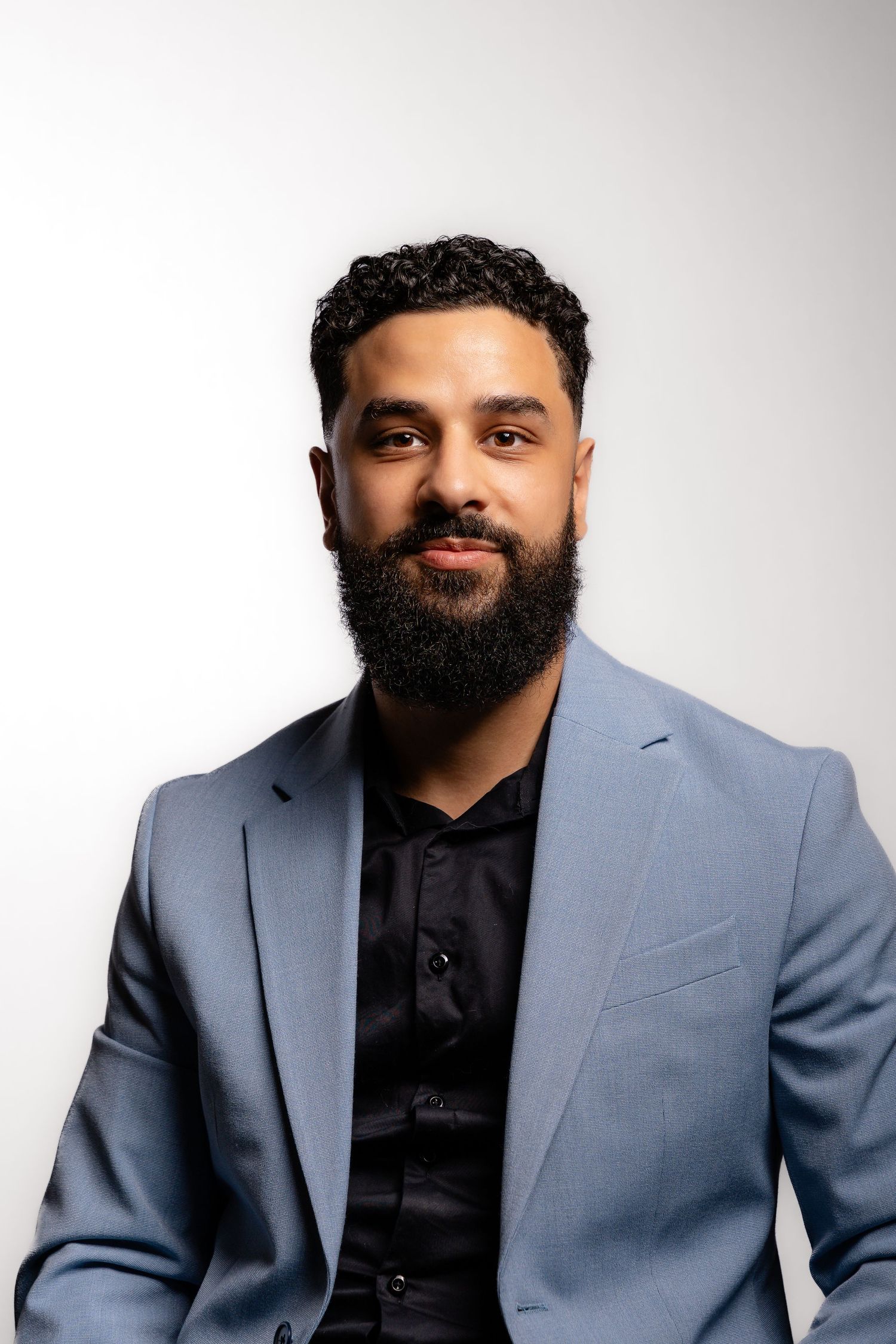 Professional studio portrait of a person wearing a gray suit jacket and black shirt against white background.
