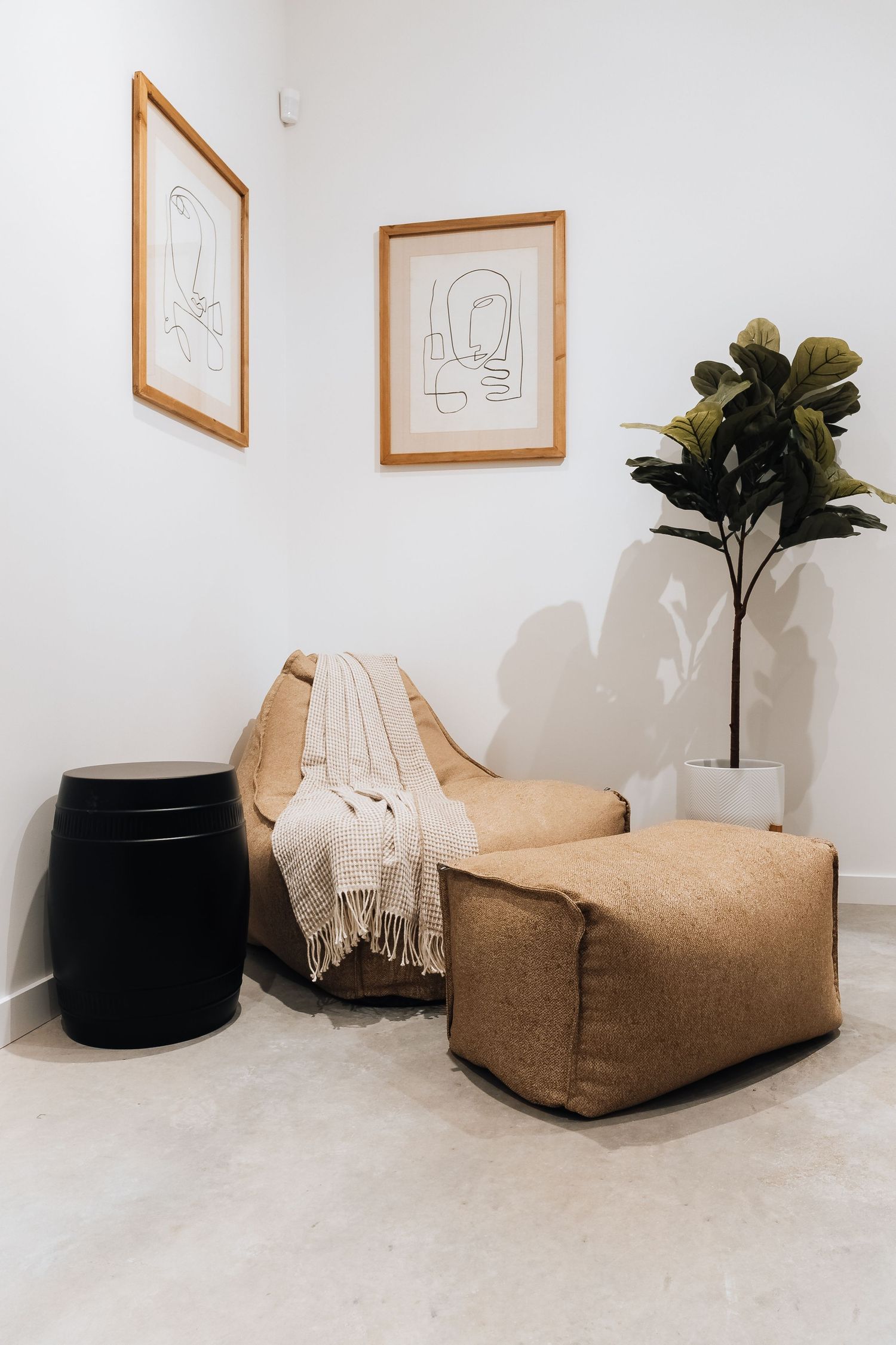 Cozy lounge area with beige bean bag chairs, framed wall art, and potted plants in a bright white room.