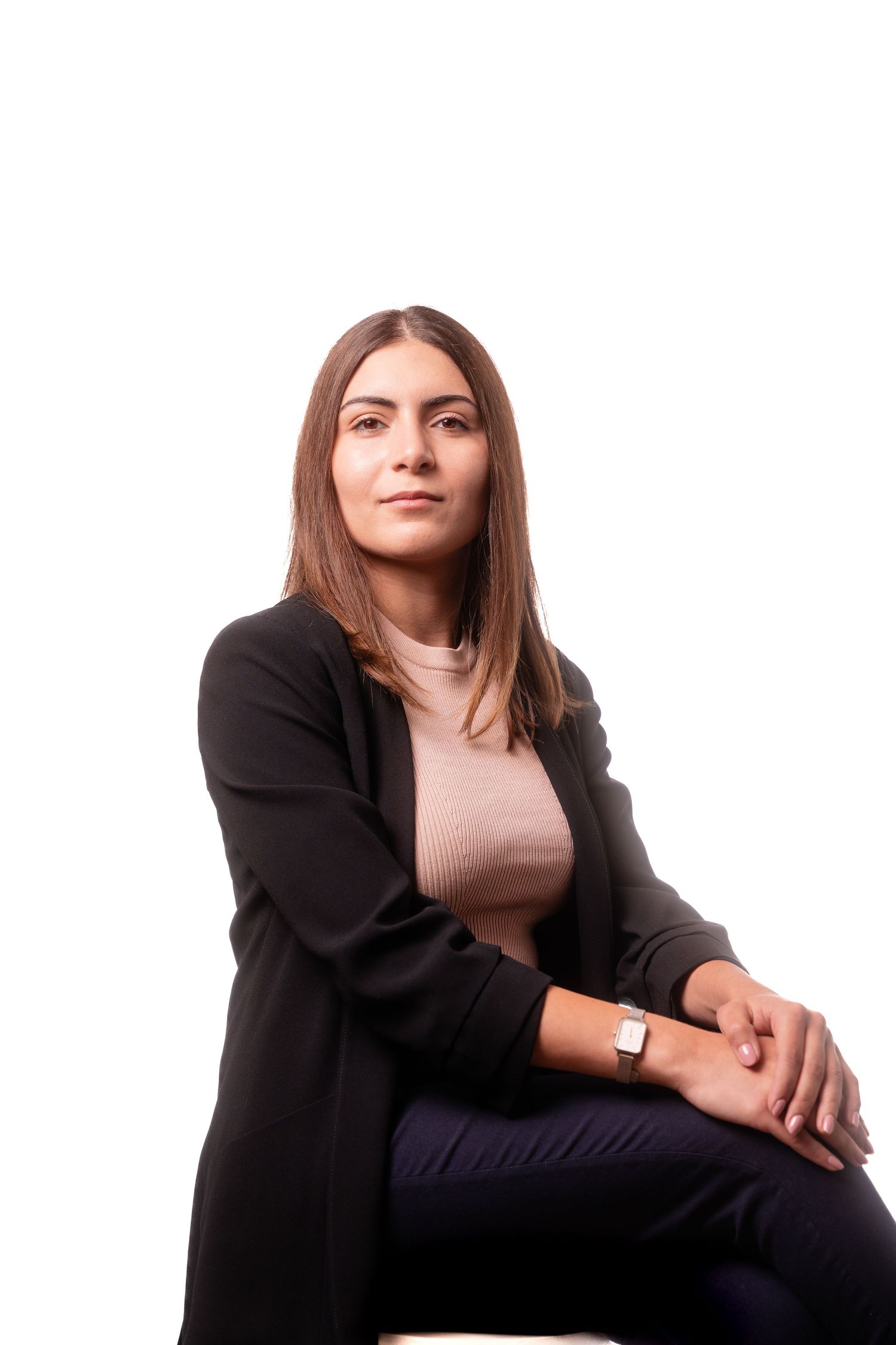 Professional portrait of person in black blazer and pink top sitting against white background.