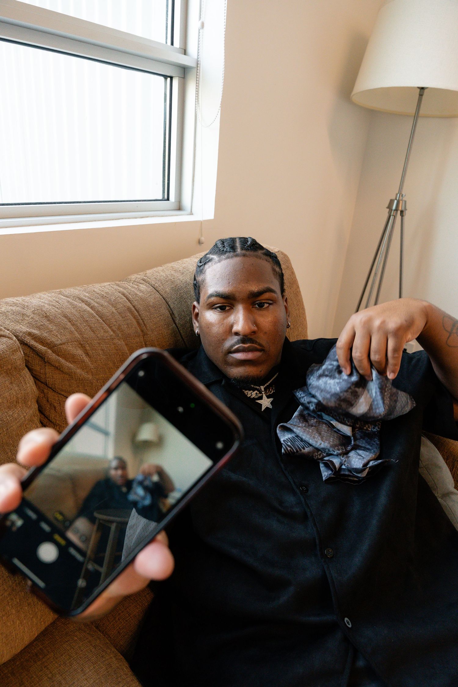 Person reclining on brown couch holding up smartphone in sunlit room.