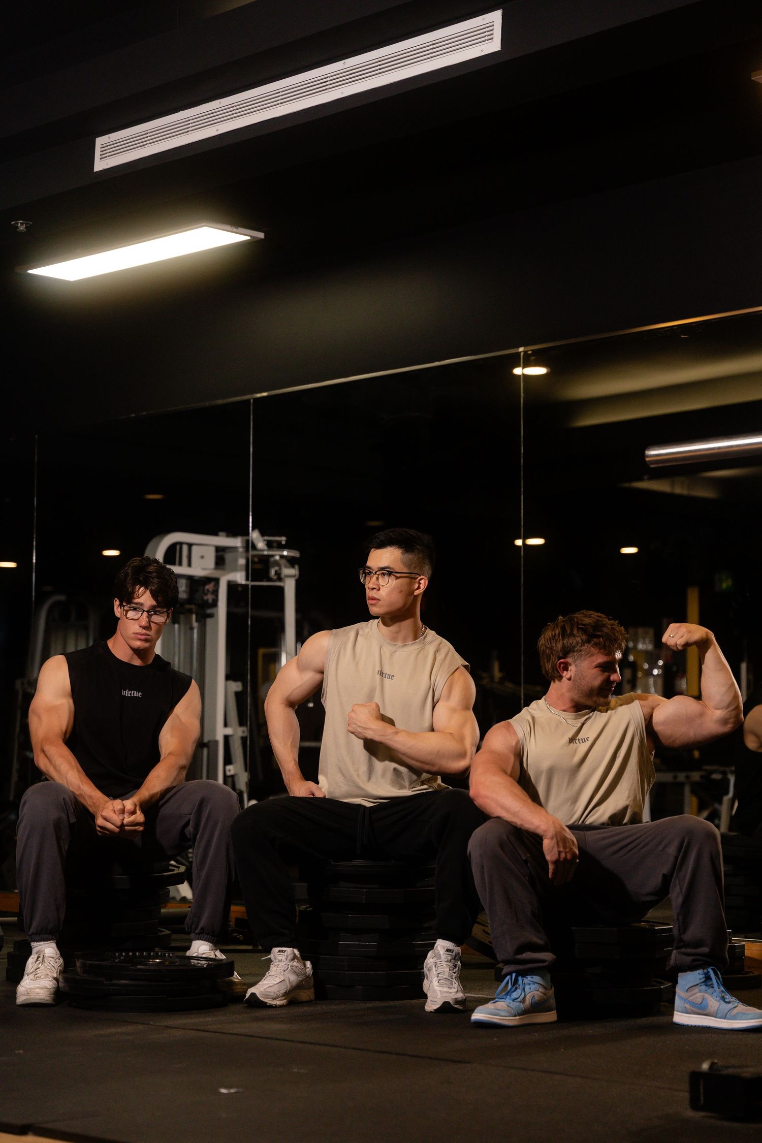 Group of people sitting and resting on gym equipment in dark atmospheric lighting.