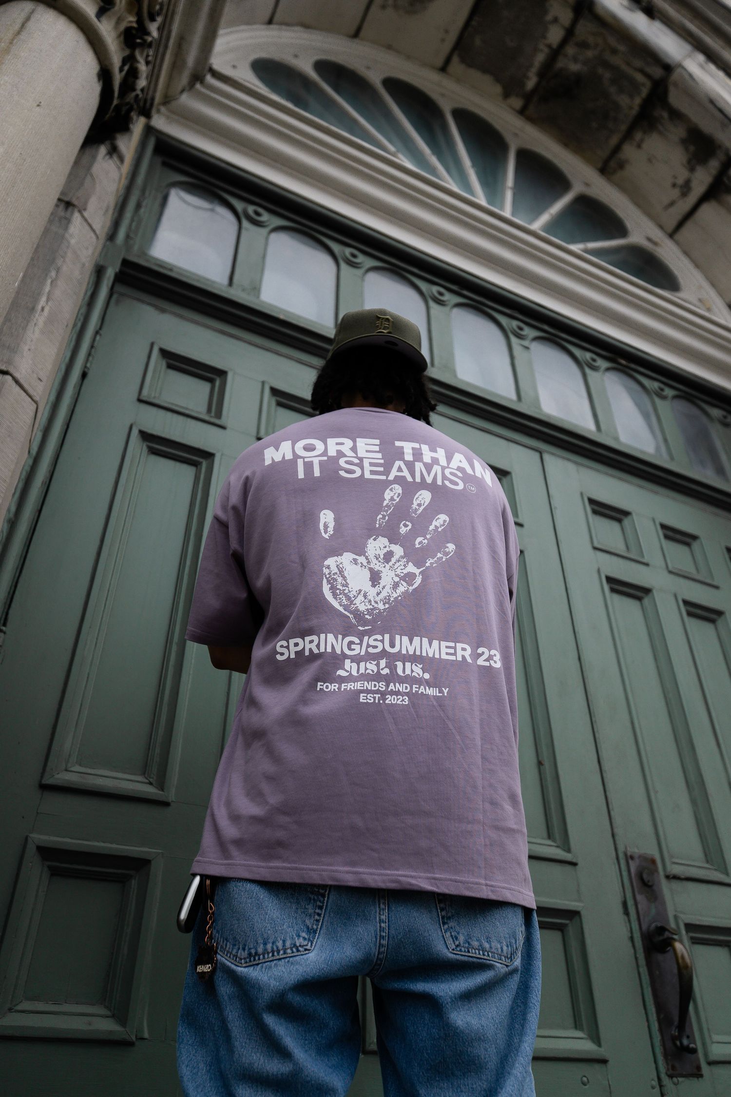 Person wearing purple graphic t-shirt photographed from behind against green doors.