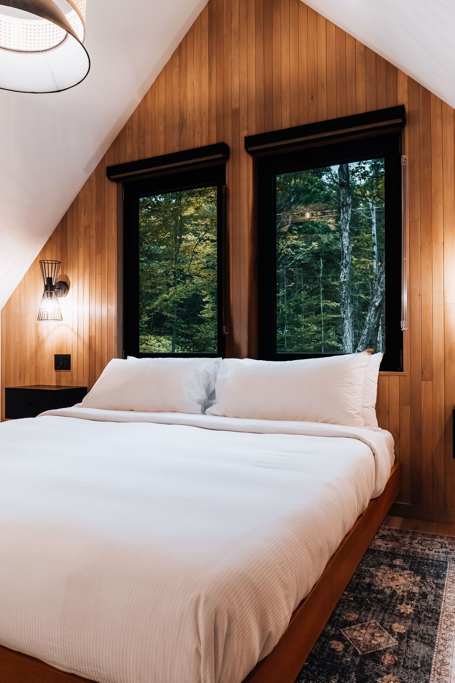 Modern bedroom featuring wood paneling, black-framed windows, and forest views.