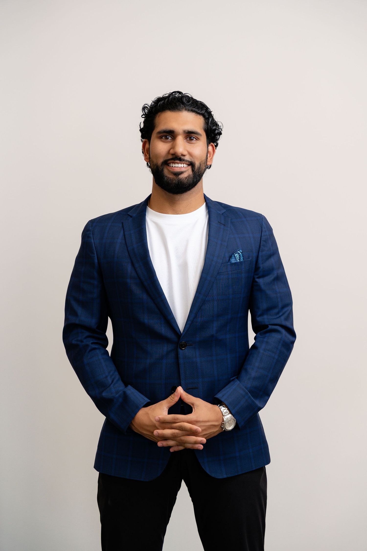 Professional in navy check blazer poses with clasped hands against white background.