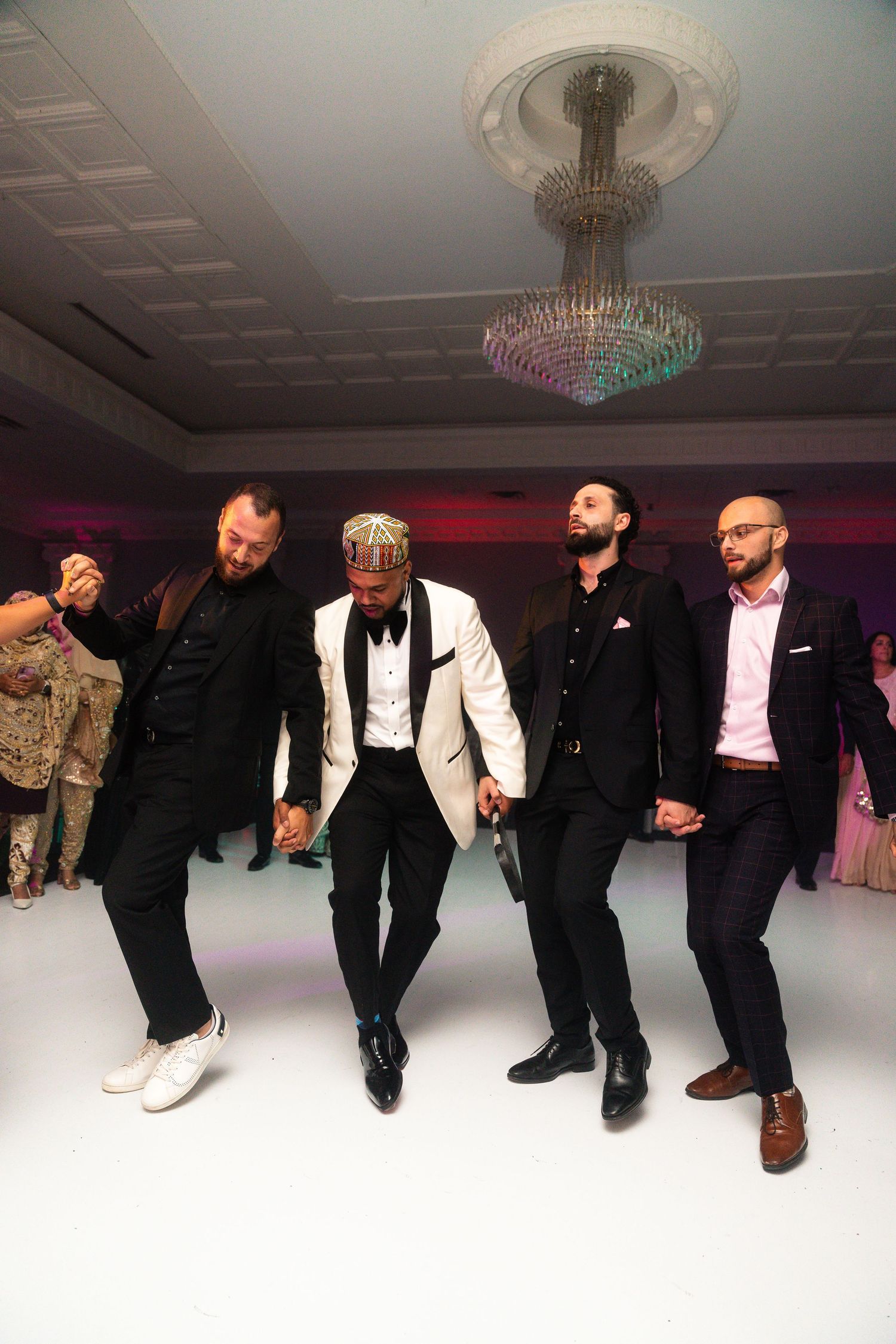 A group of people in formal black and white attire photographed from the waist down on a white dance floor.