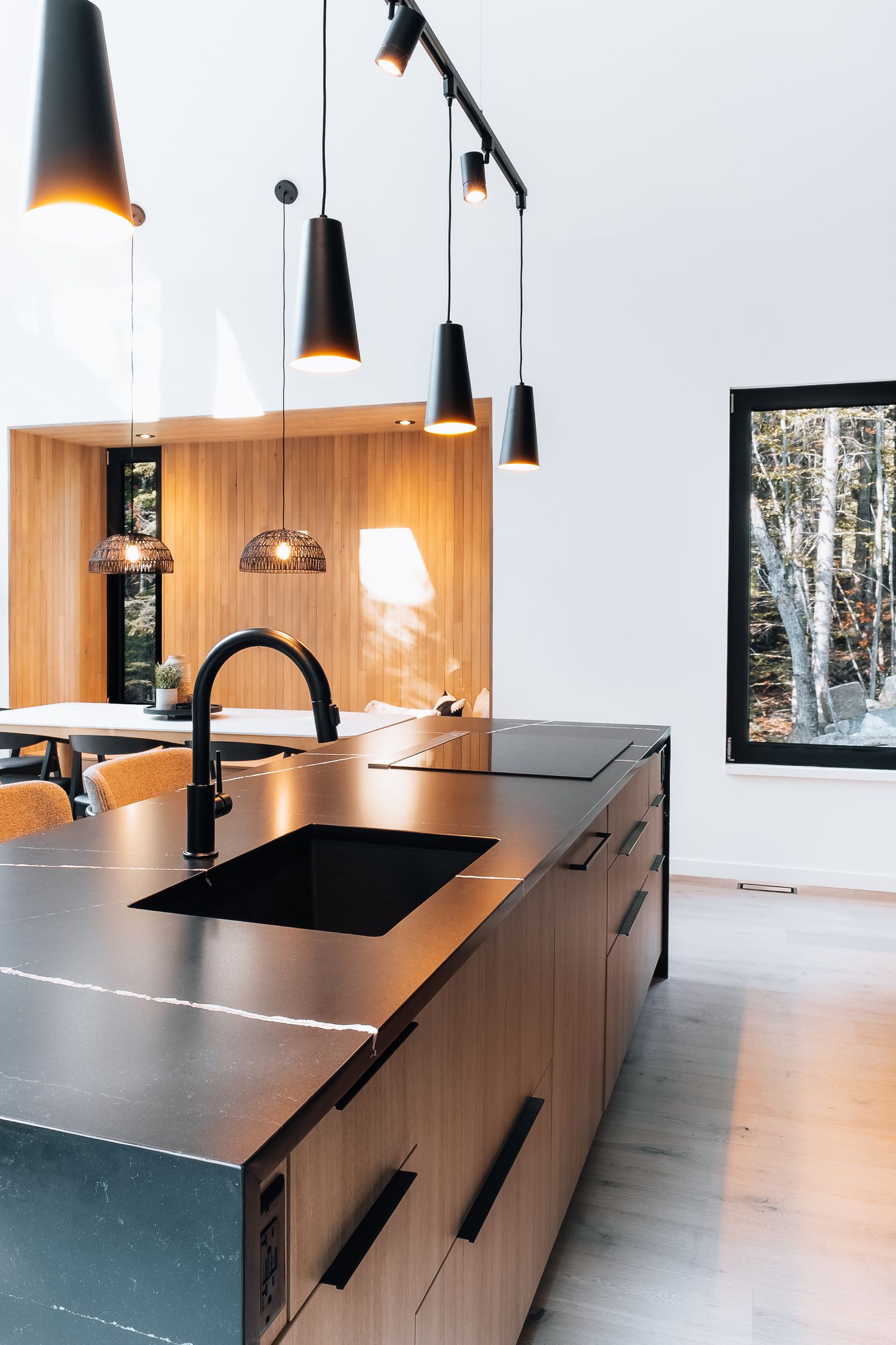 Modern kitchen with black pendant lights, wooden cabinets, and stainless steel countertops.