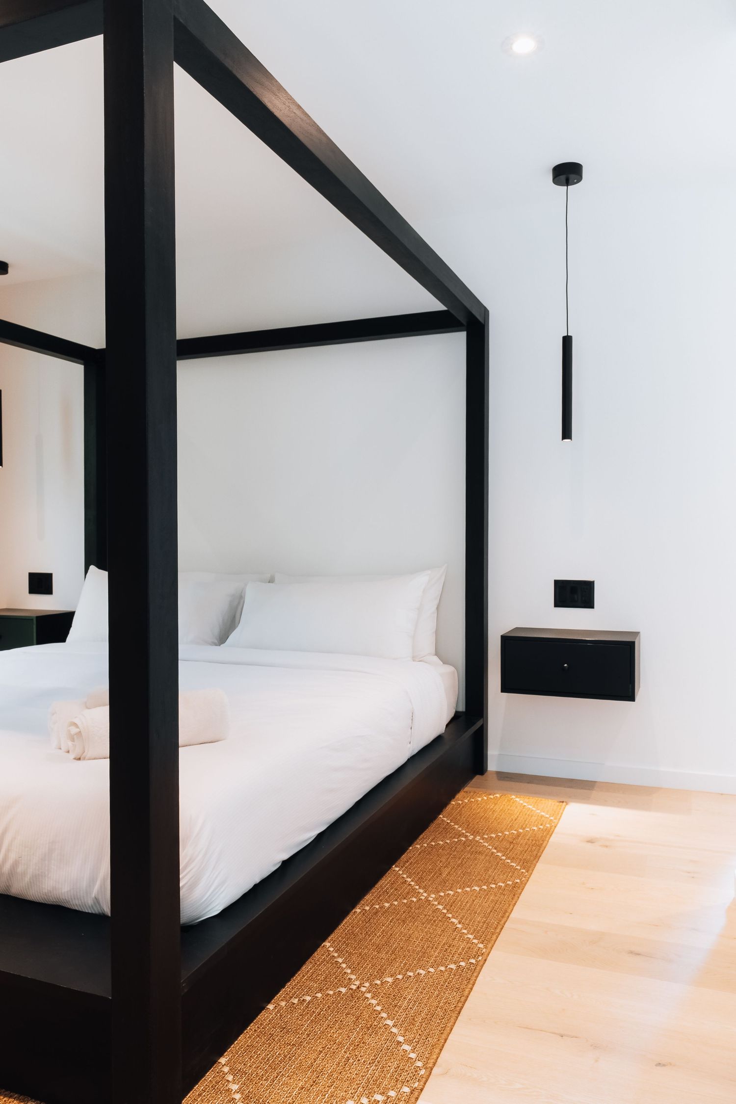 Modern bedroom with black structural beams and geometric patterned rug on light wood flooring.