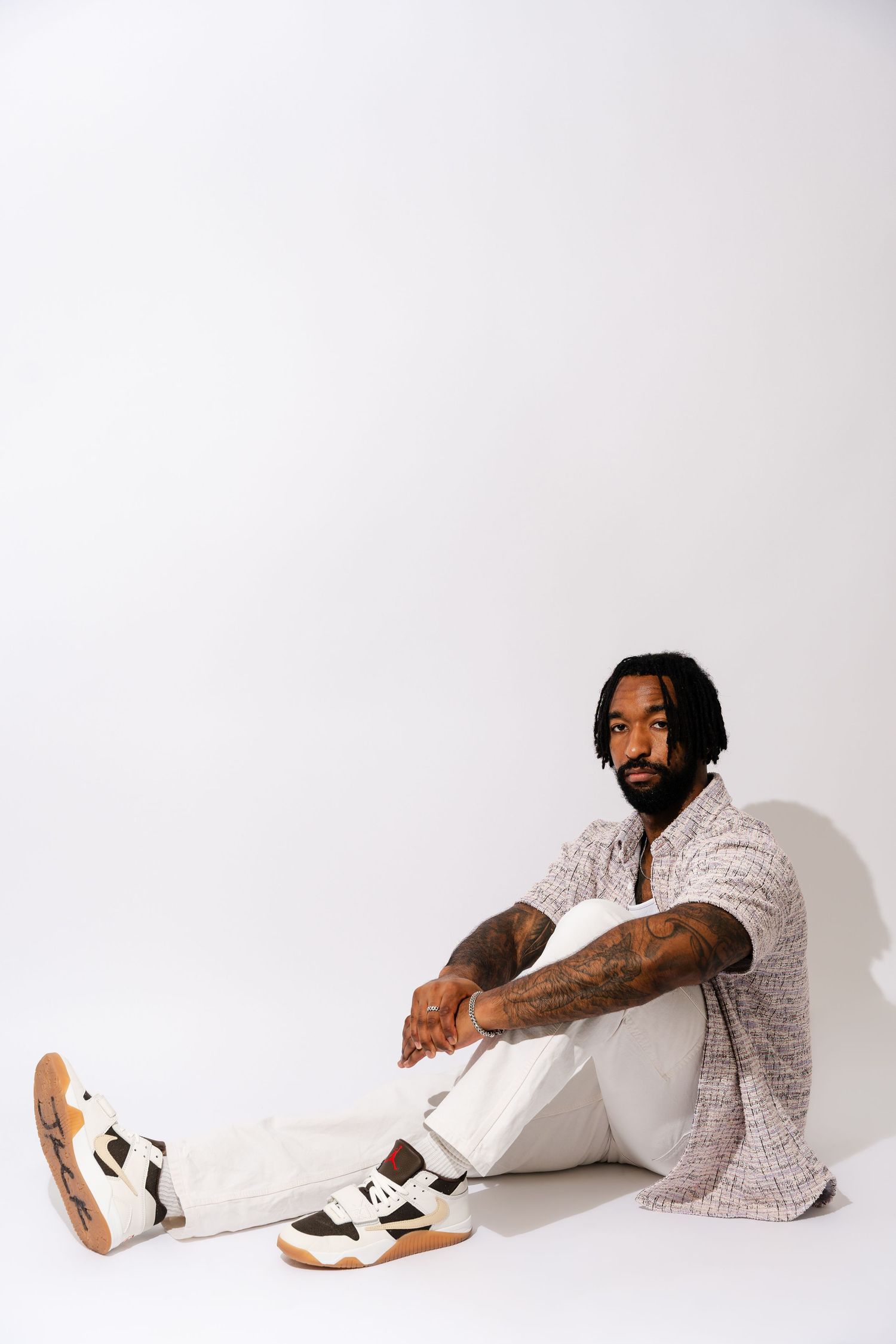 Person in patterned shirt and white pants reclines on white floor showcasing athletic footwear.