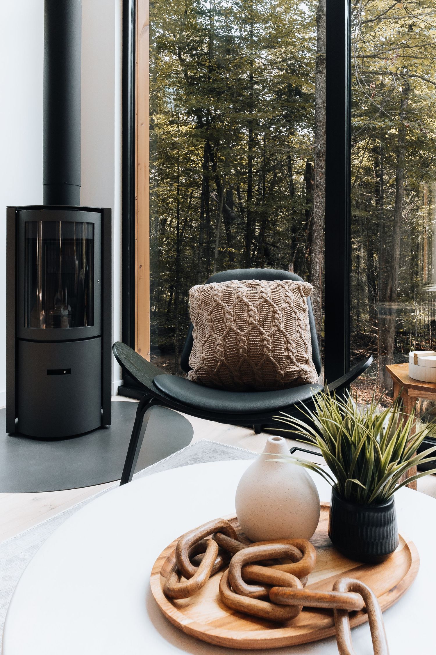 Decorative items displayed on white counter with black wood stove and forest view through large windows.