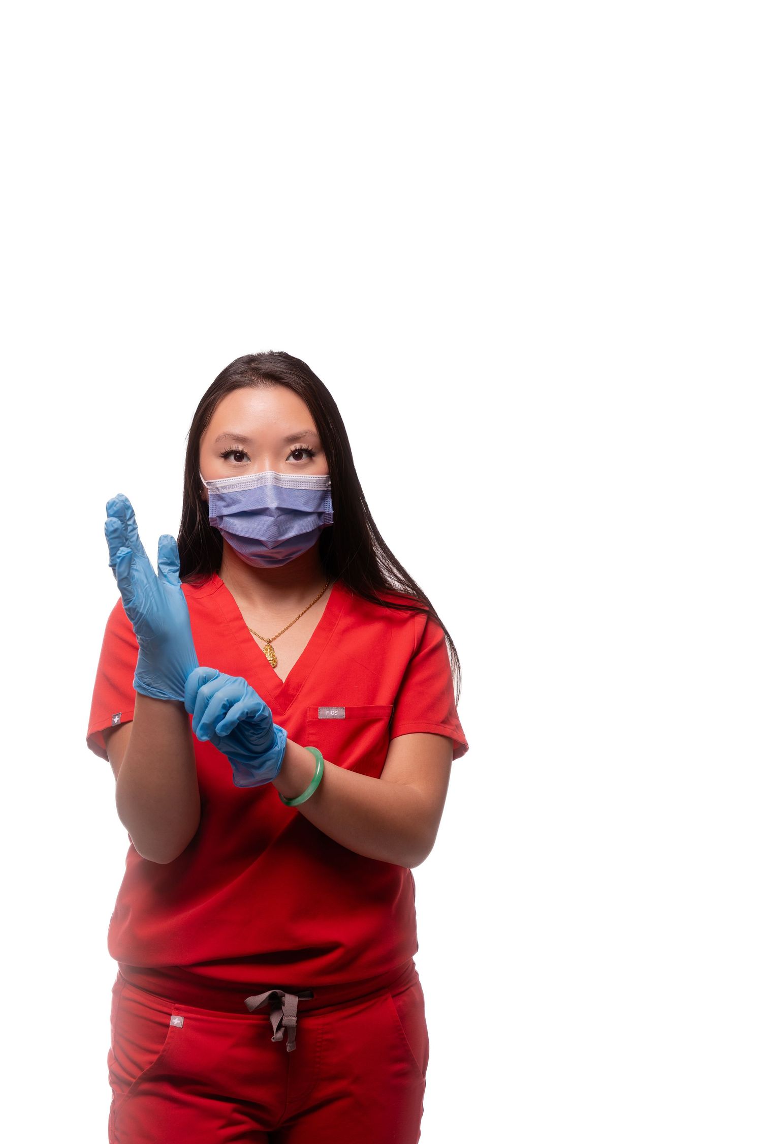 Medical professional in red scrubs and protective gear gestures while wearing face mask.
