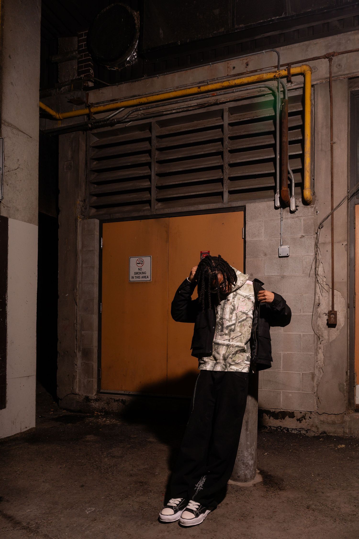 Streetwear outfit photographed in dimly lit industrial loading zone.