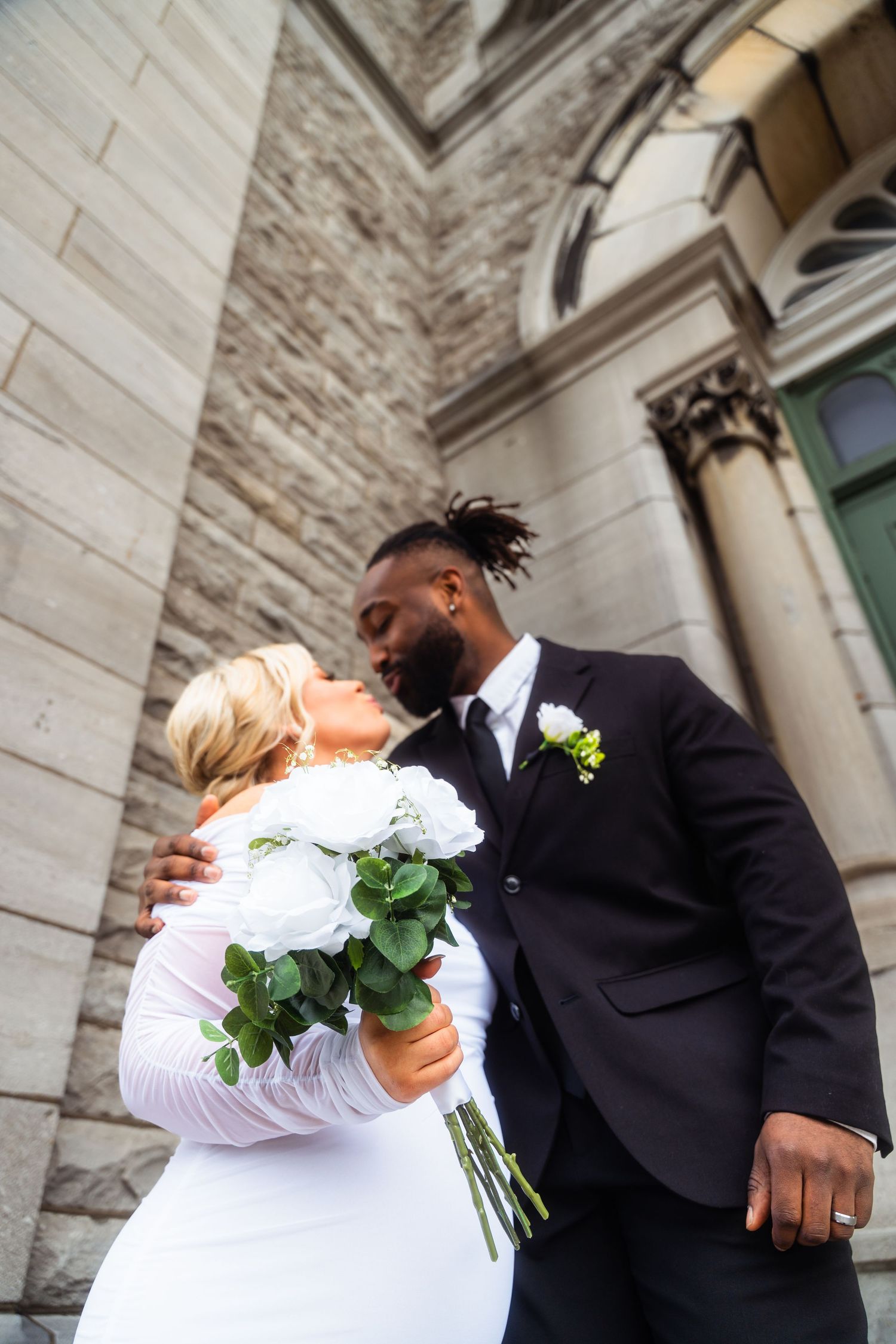Candid wedding photo showing couple's intimate moment on church steps with white bouquet.