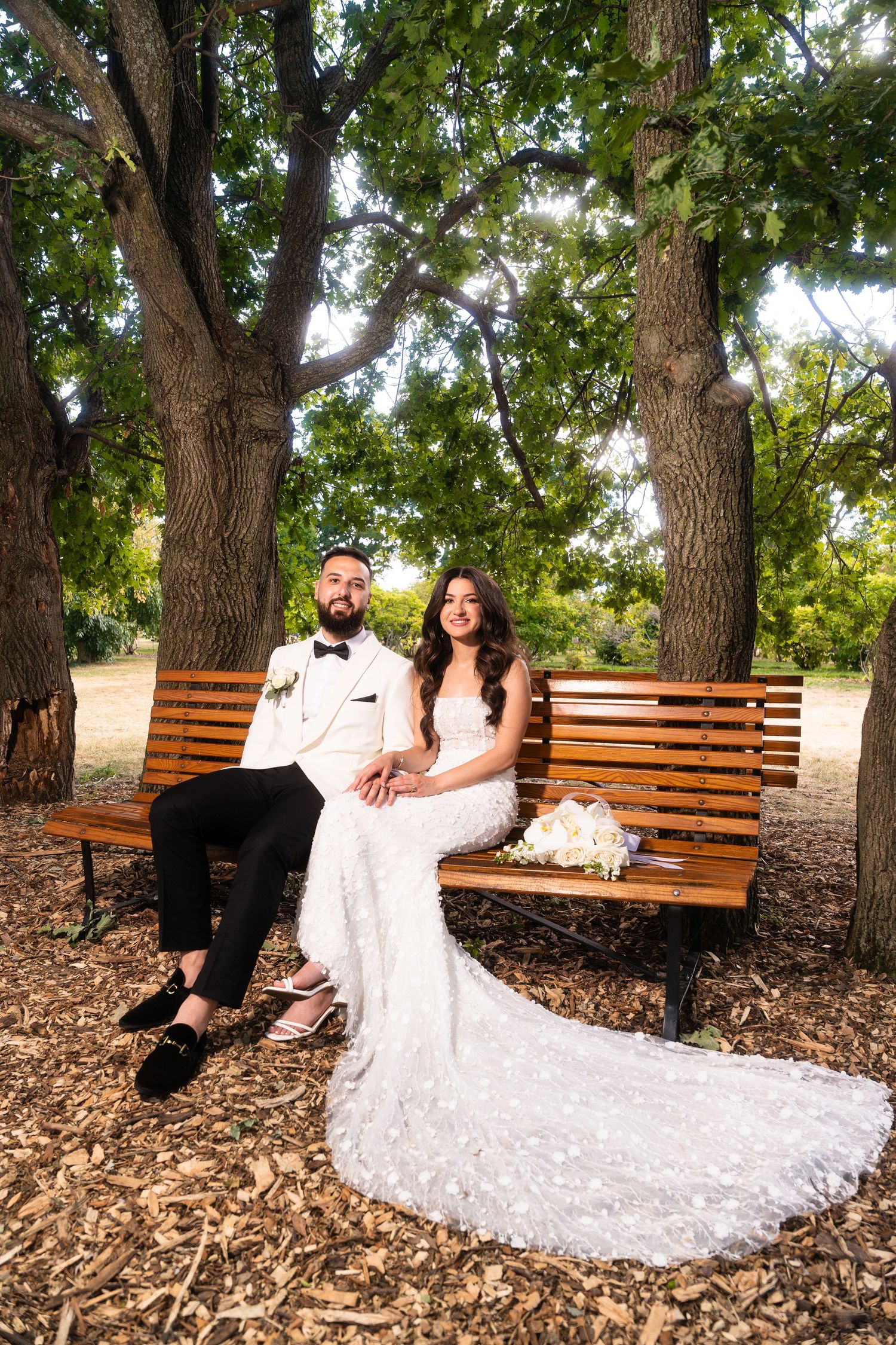Romantic wedding photos on wooden bench with bride's dress elegantly displayed.