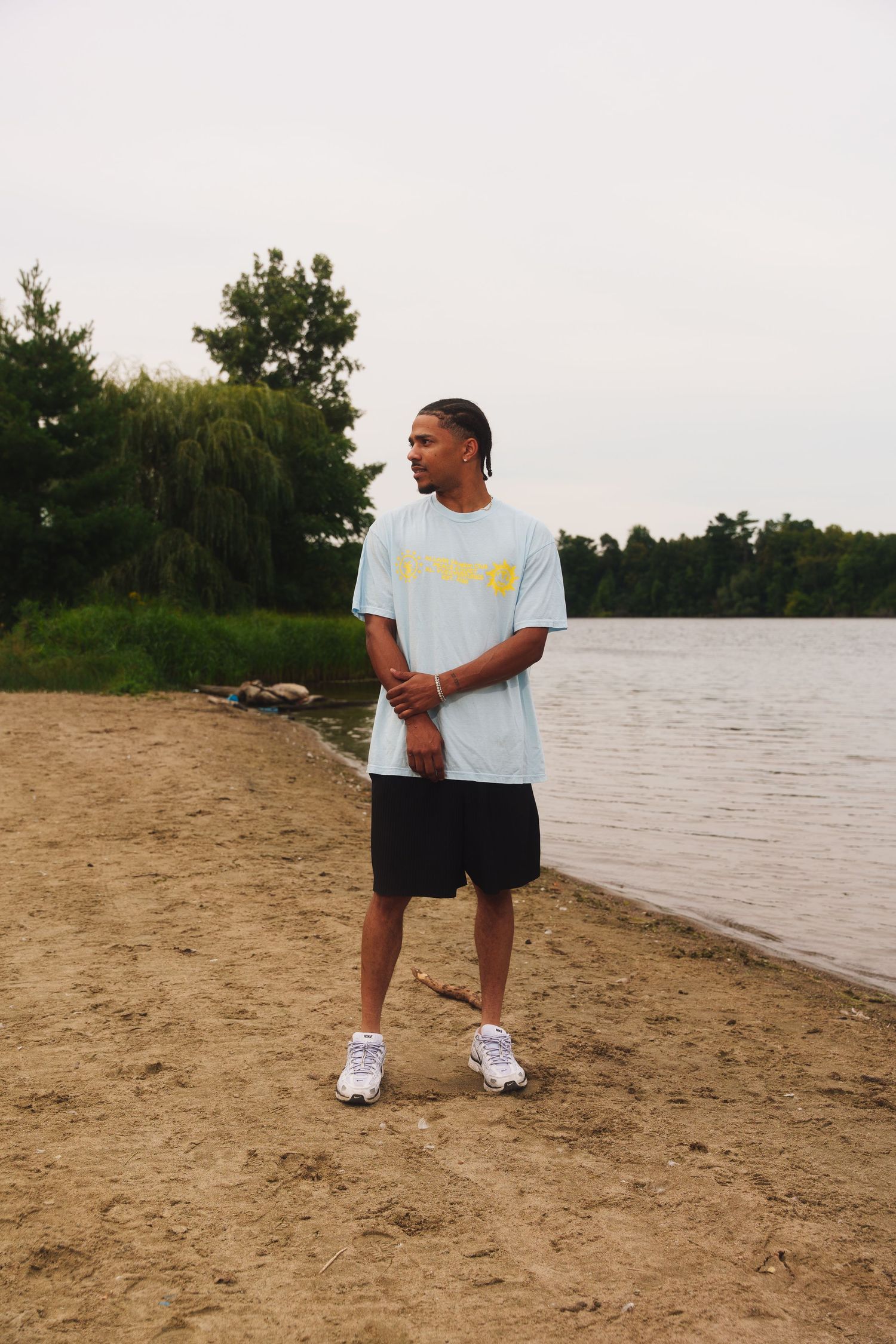 Person in white t-shirt and black shorts standing on beach near water.