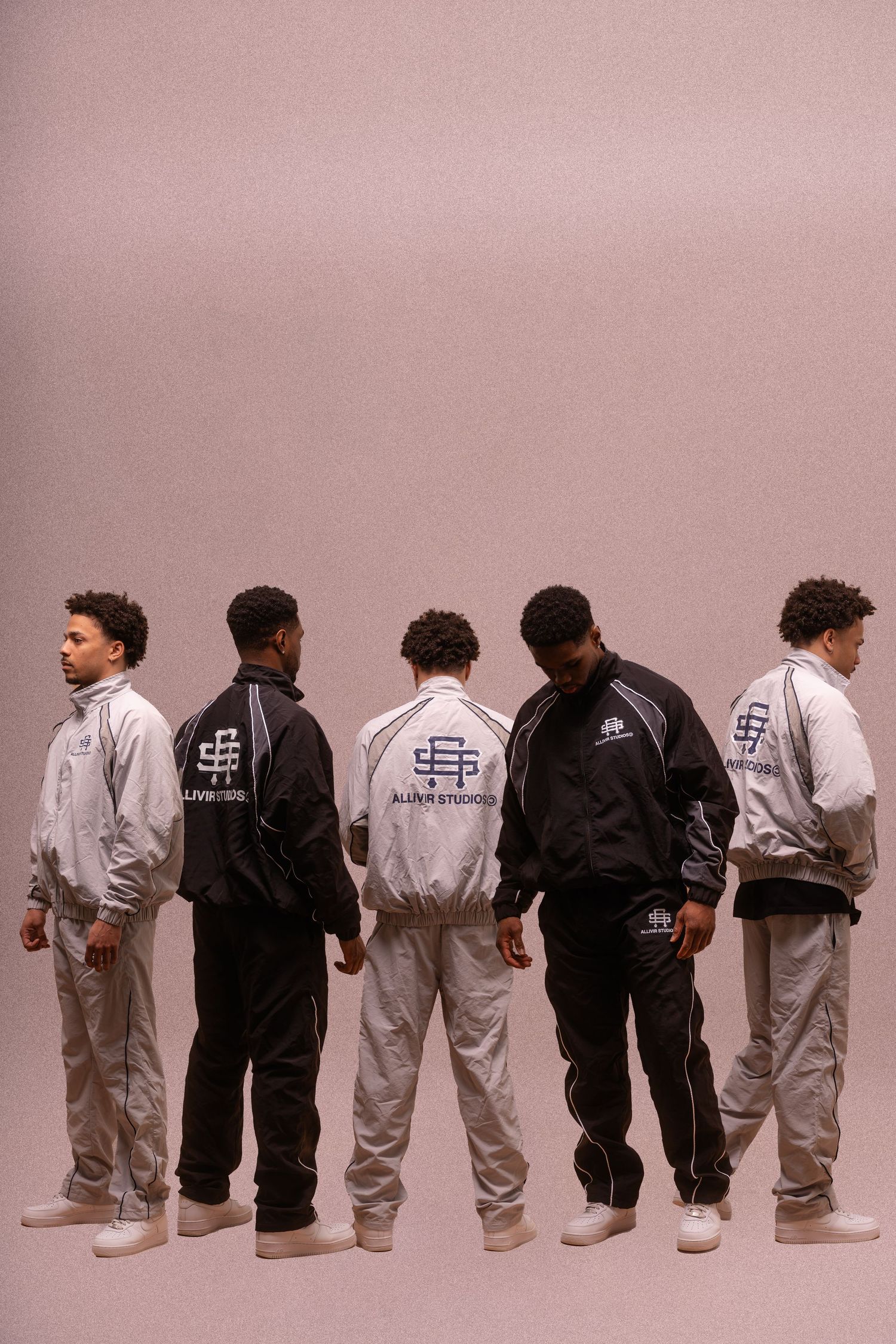 A lineup of people wearing black and white tracksuits standing against a pink background.