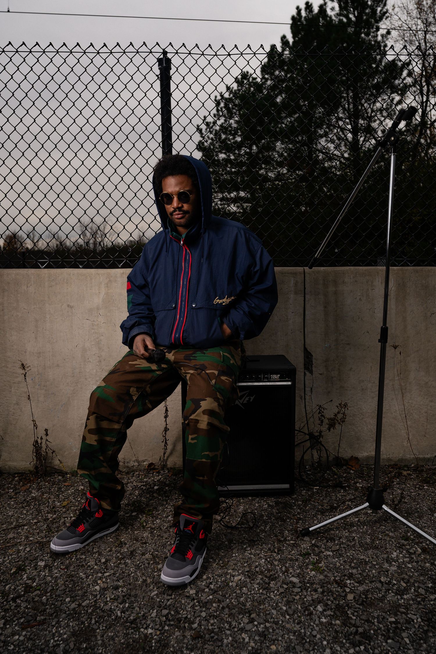 Person in casual wear sitting against concrete wall with chain link fence.