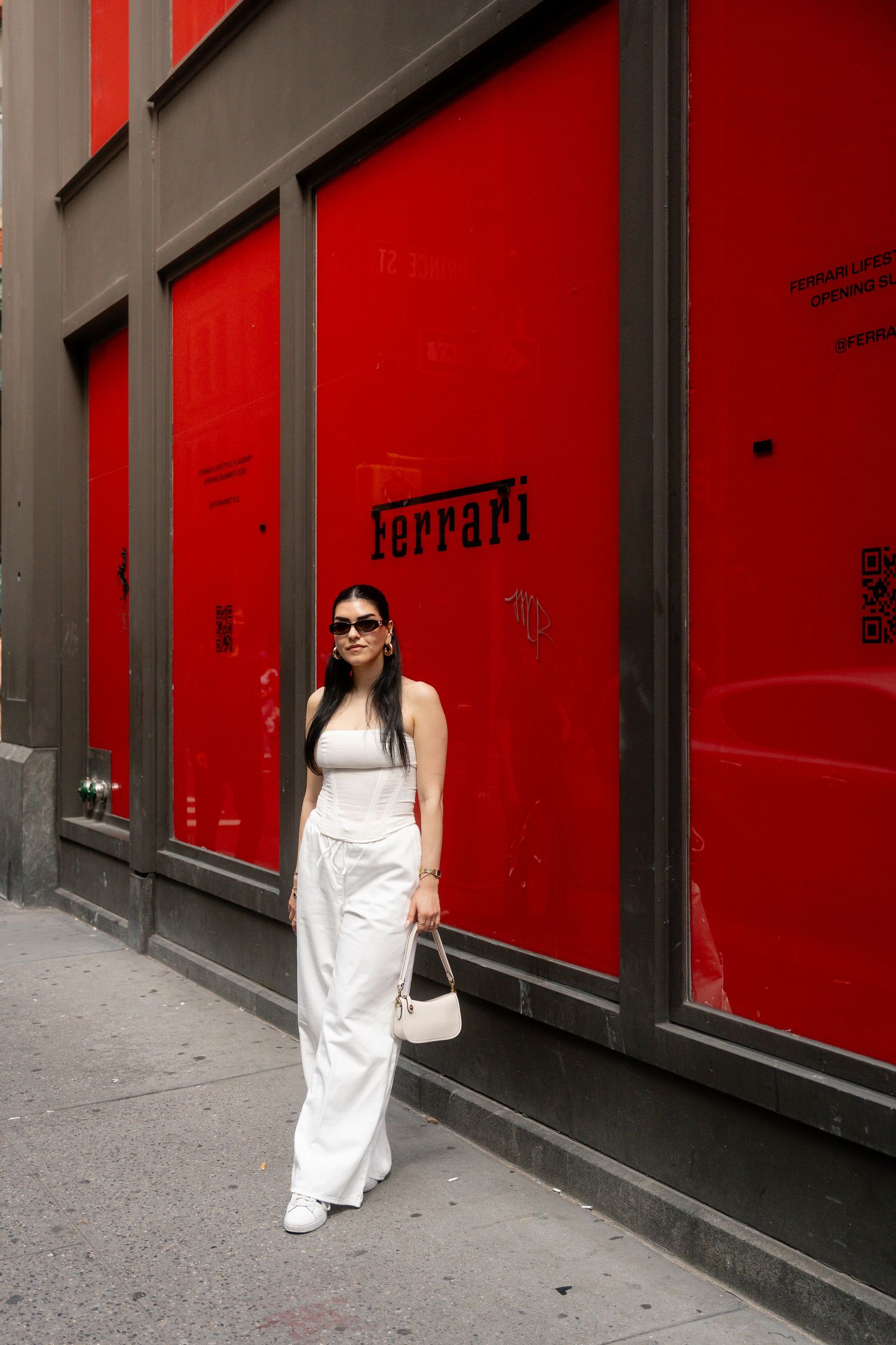 Figure in white dress walks past bright red Ferrari storefront windows.