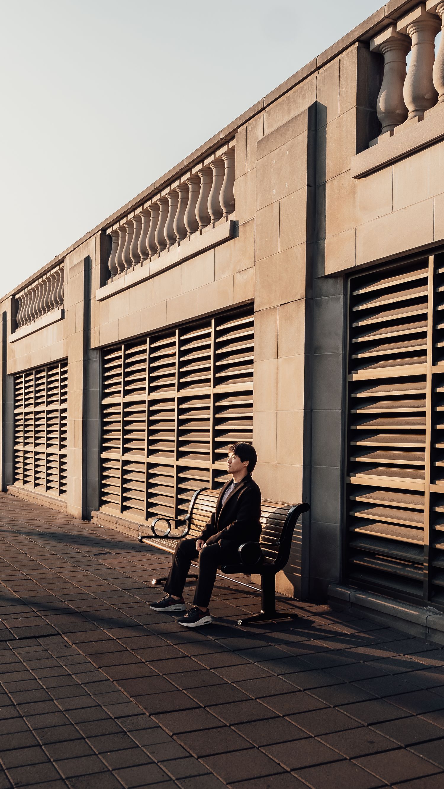 Urban architectural scene with repeating louvered windows and person sitting against wall.