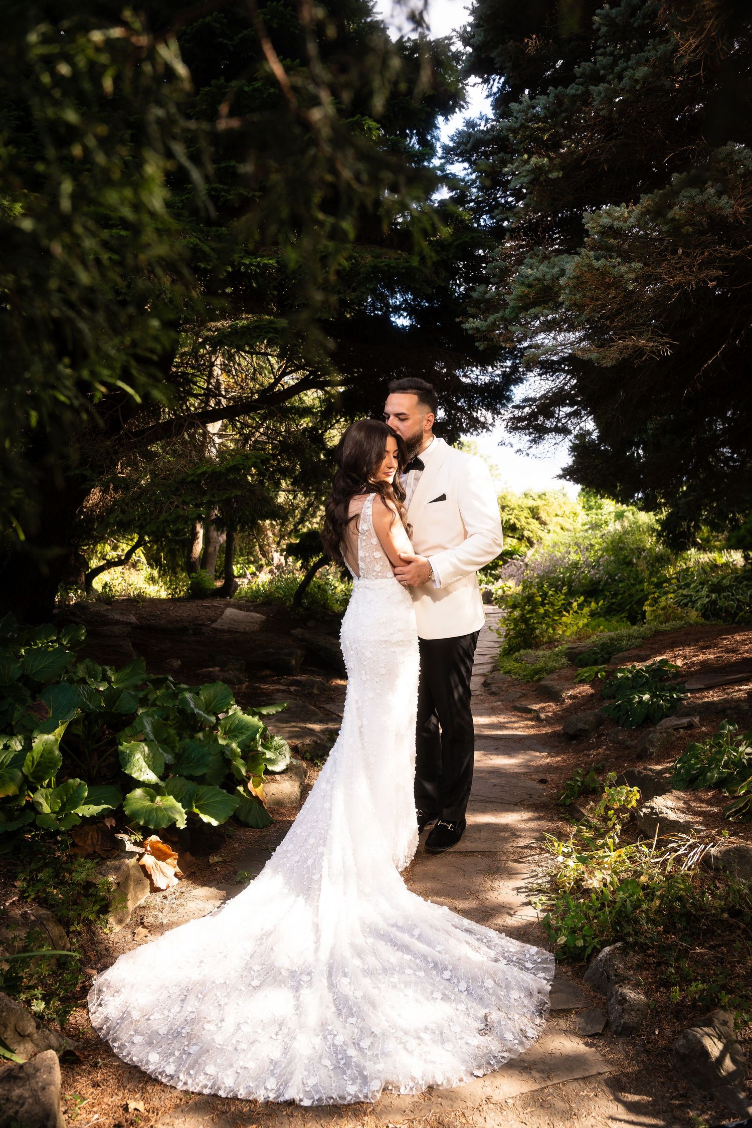 Wedding couple dancing in sunlit garden path surrounded by lush greenery.