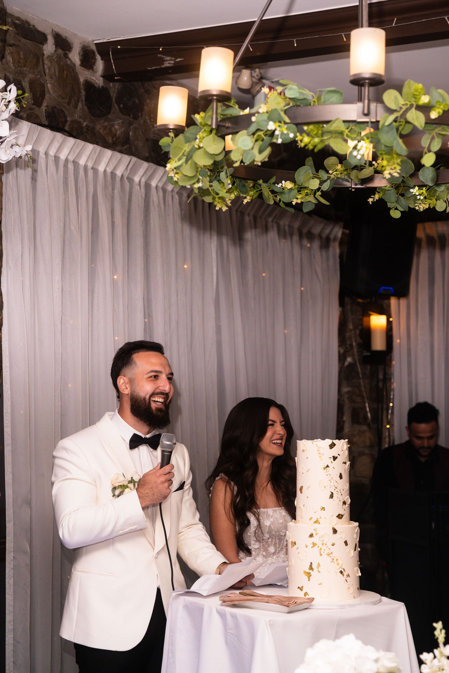 A couple shares a joyful moment during their wedding reception while standing next to their elegant white wedding cake.