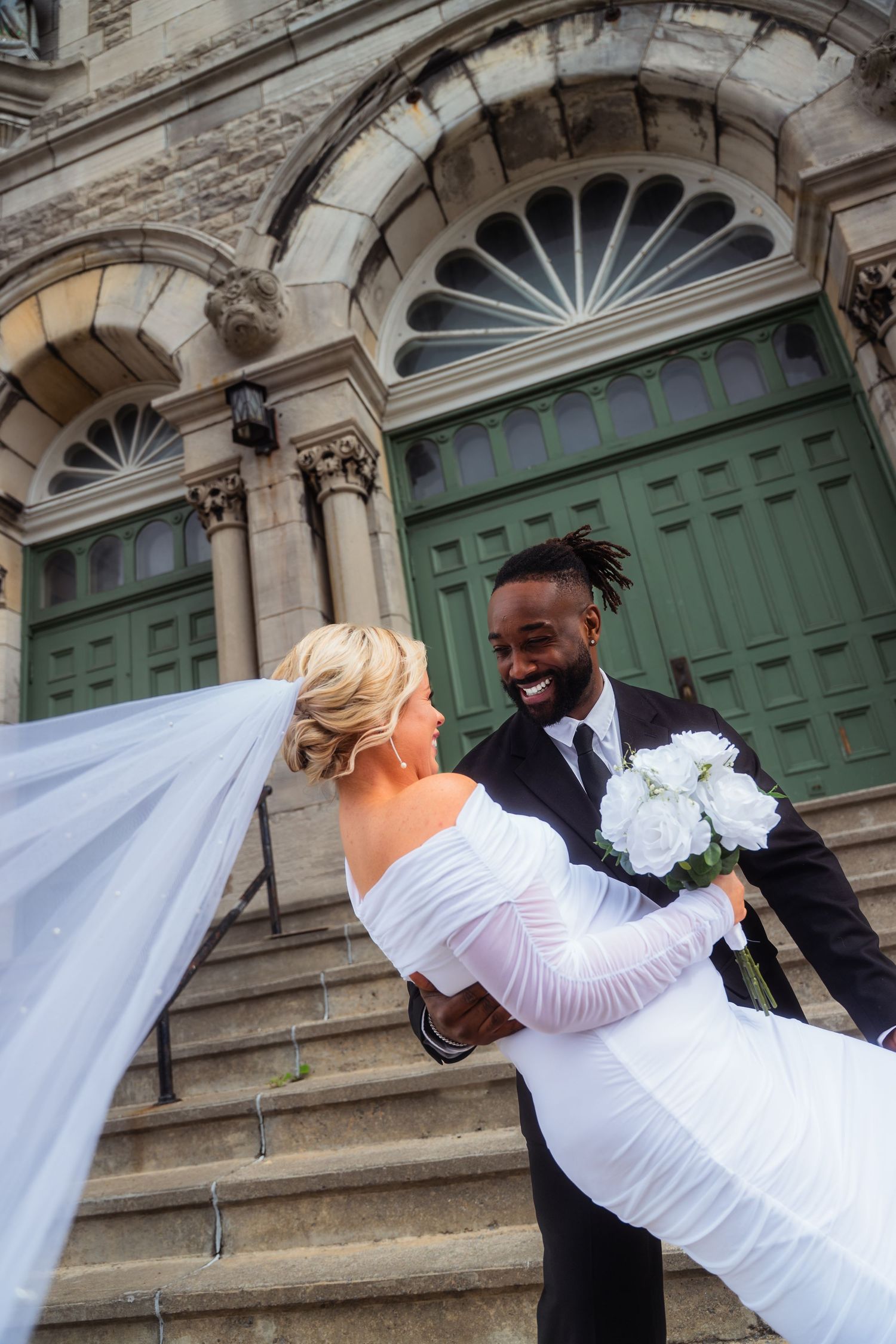 A wedding couple shares a romantic dip pose in front of historic green doors with ornate architectural details.