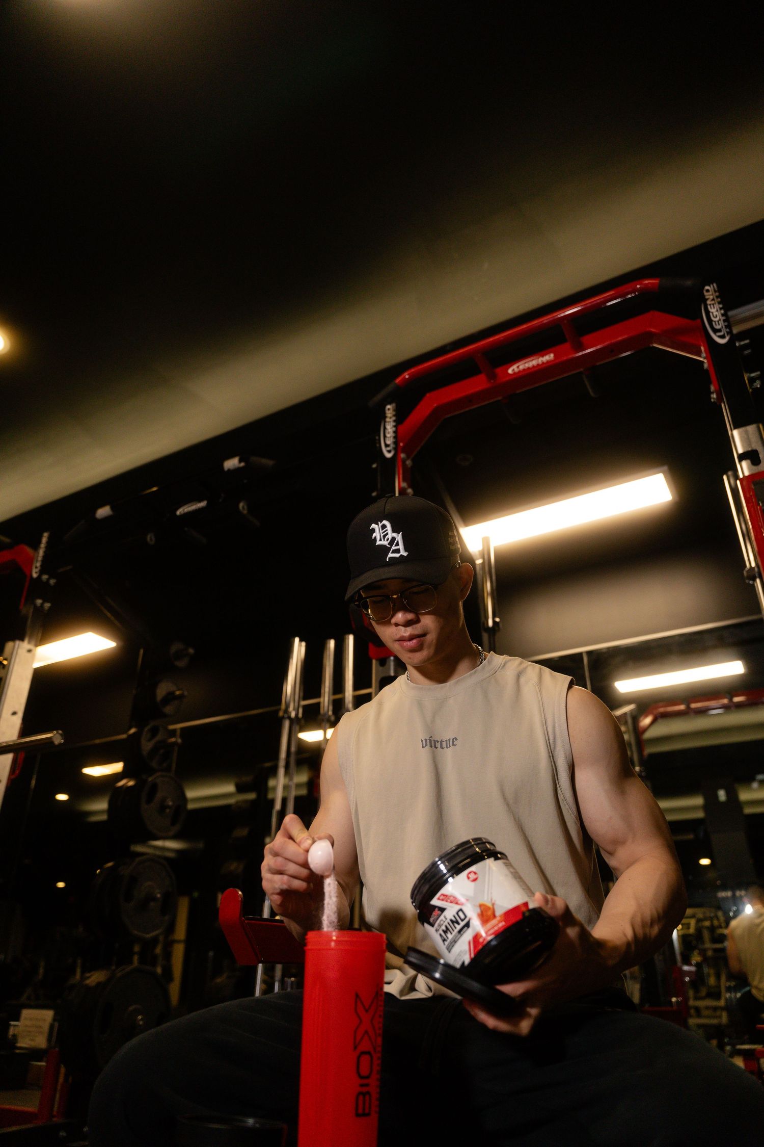 Person in white tank top handling gym equipment in dimly lit fitness facility.