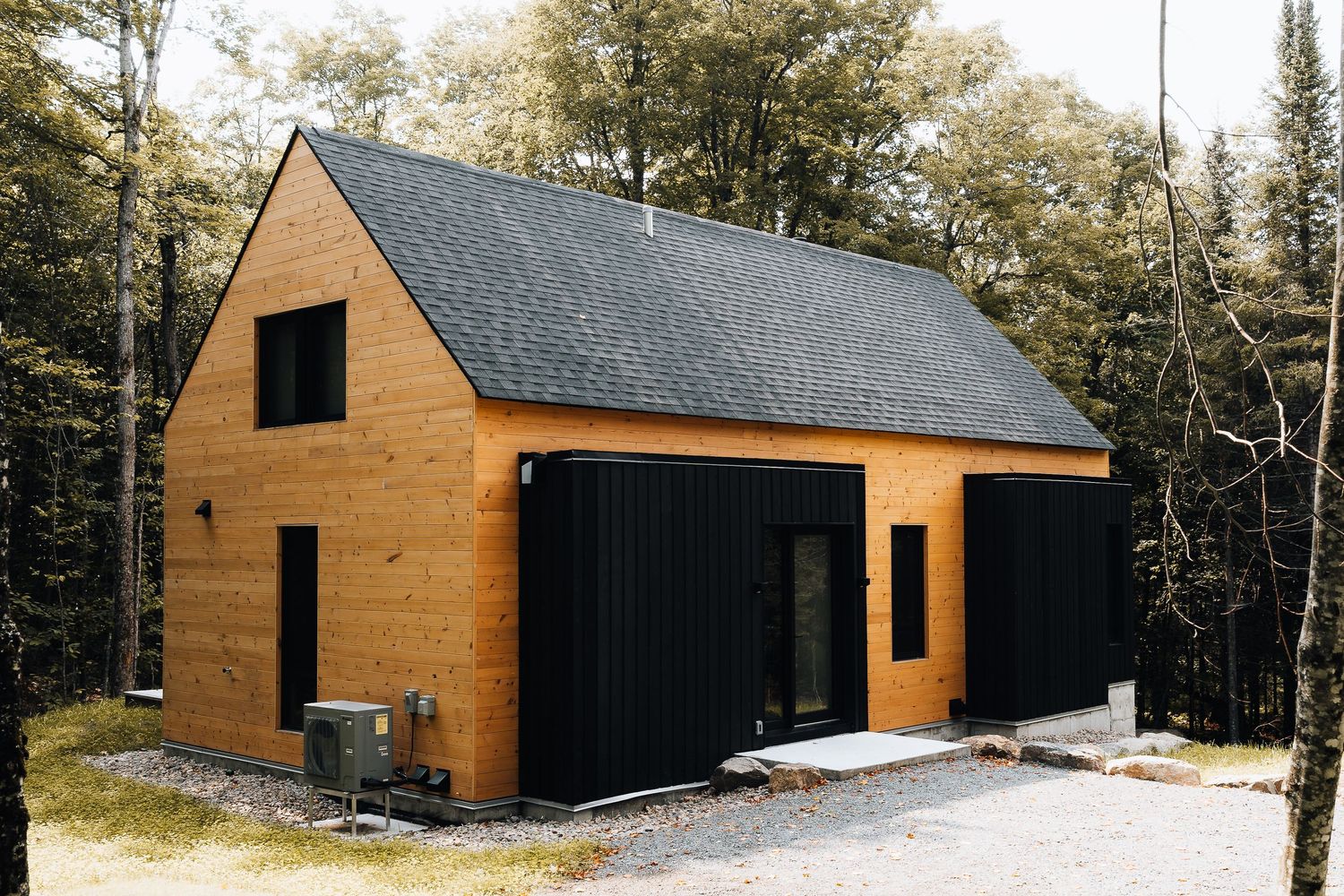 Contemporary wooden cabin with black trim and gabled roof in forest setting.