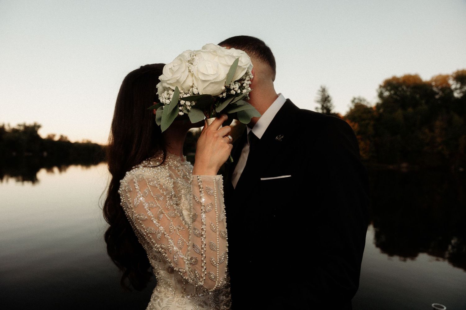 Romantic outdoor wedding portrait silhouetted against sunset sky.