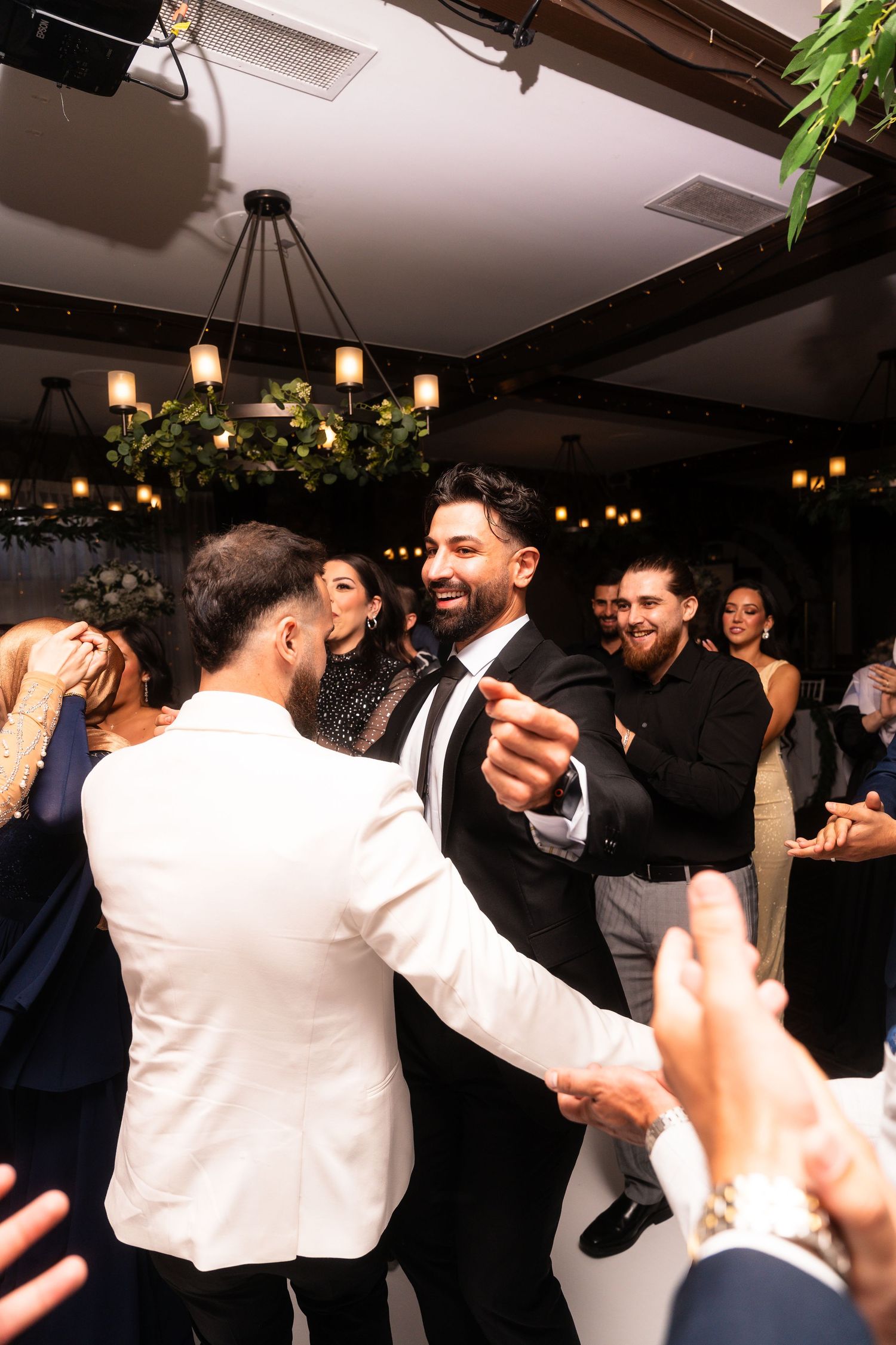 Wedding guests dancing and celebrating on a dimly lit dance floor with decorative lighting.