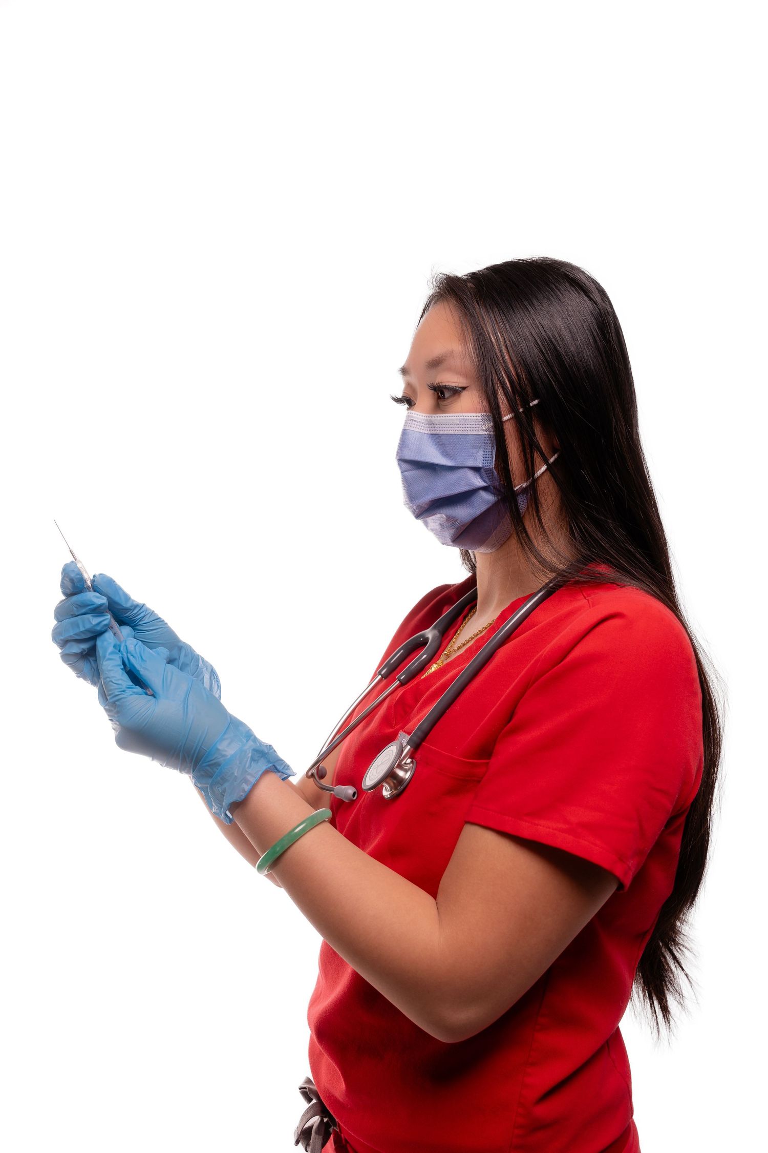 Healthcare worker in red scrubs wearing mask and gloves prepares medical equipment.