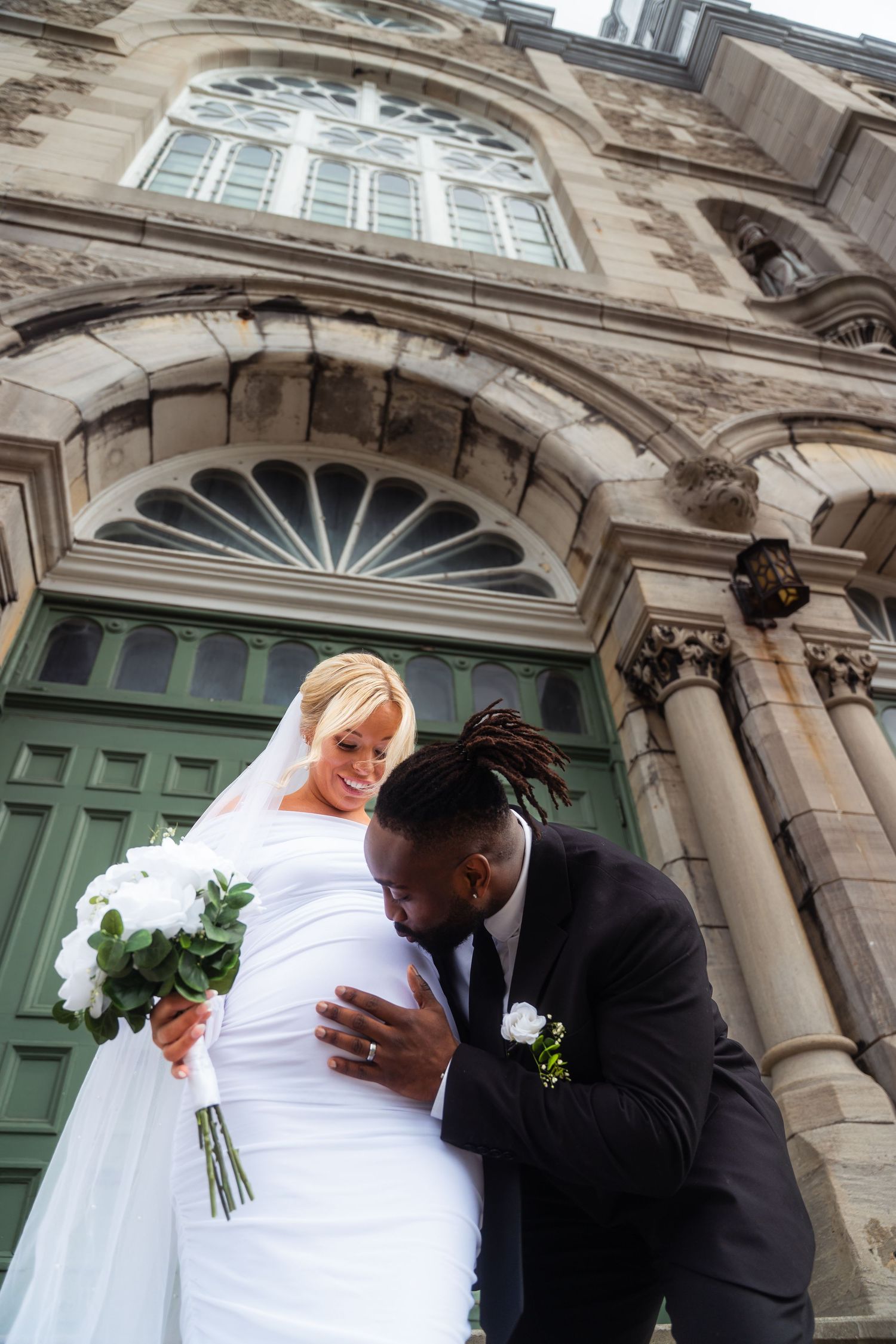 Newlywed couple sharing intimate moment outside historic stone building with arched doorway.