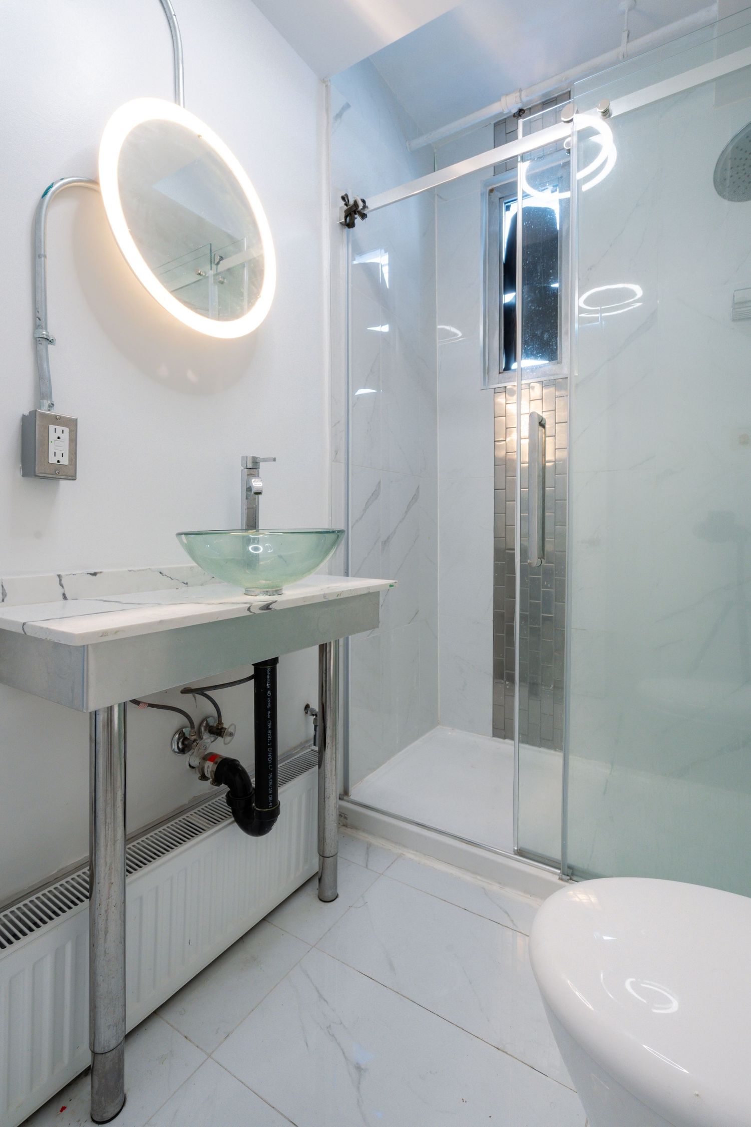 Contemporary bathroom interior with circular LED mirror and glass shower partition.