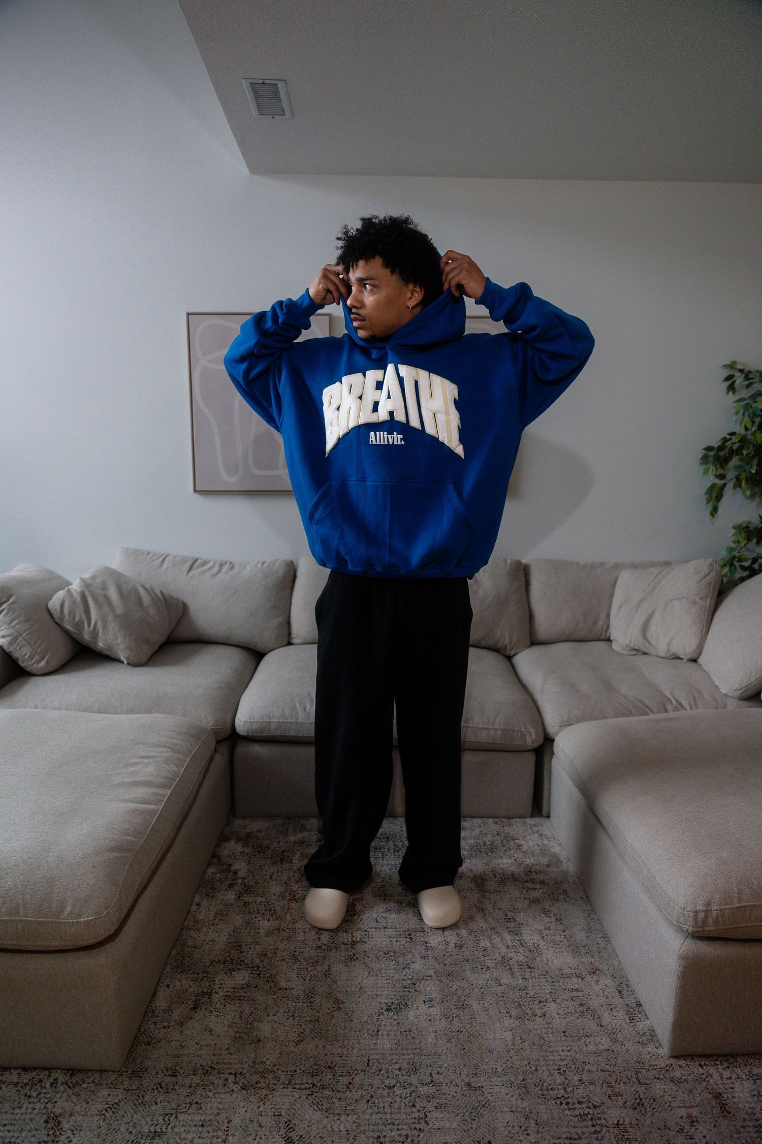 Person in blue hoodie posing in front of gray sectional sofa.