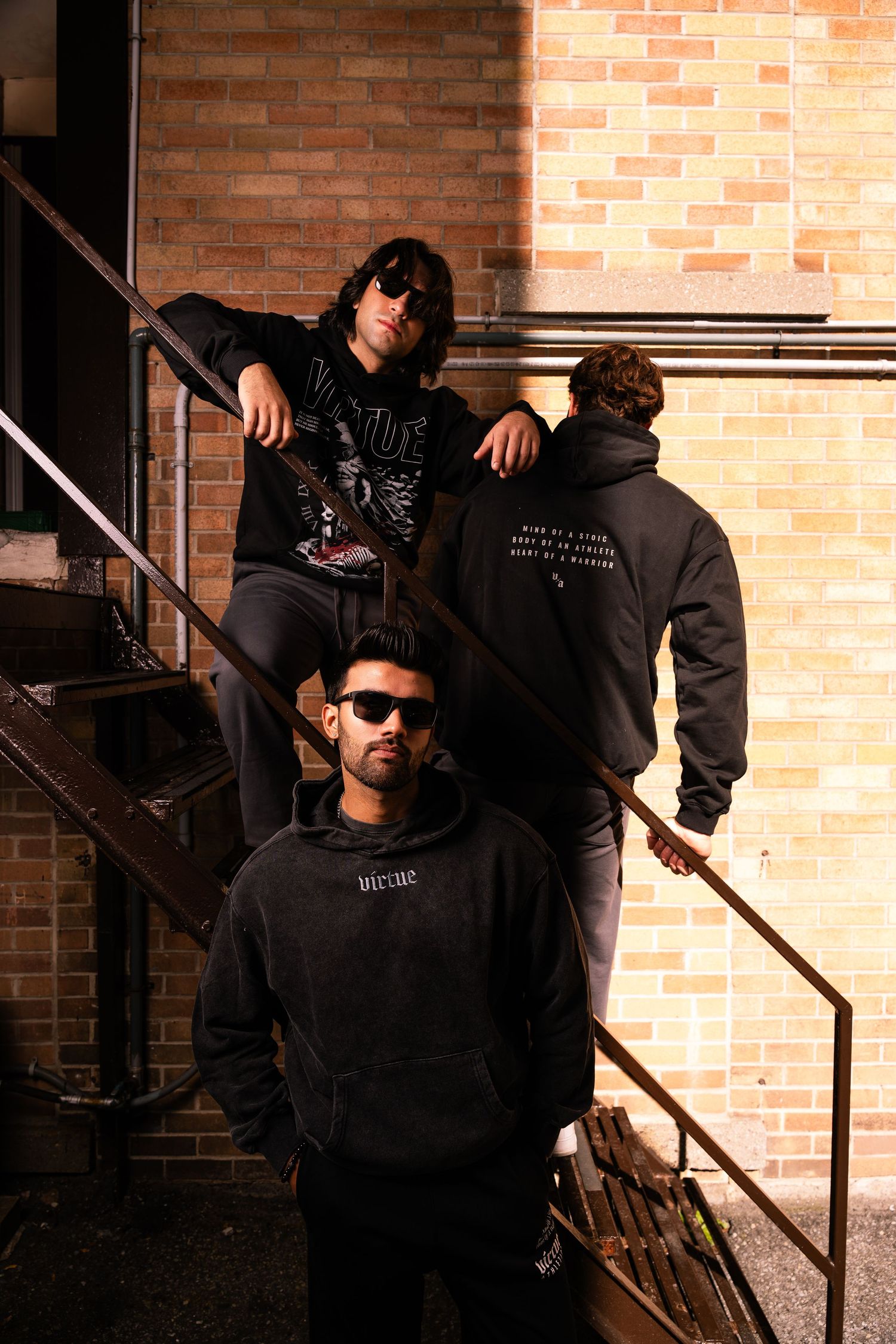 Urban fashion shoot featuring models in black hoodies on metal stairs.