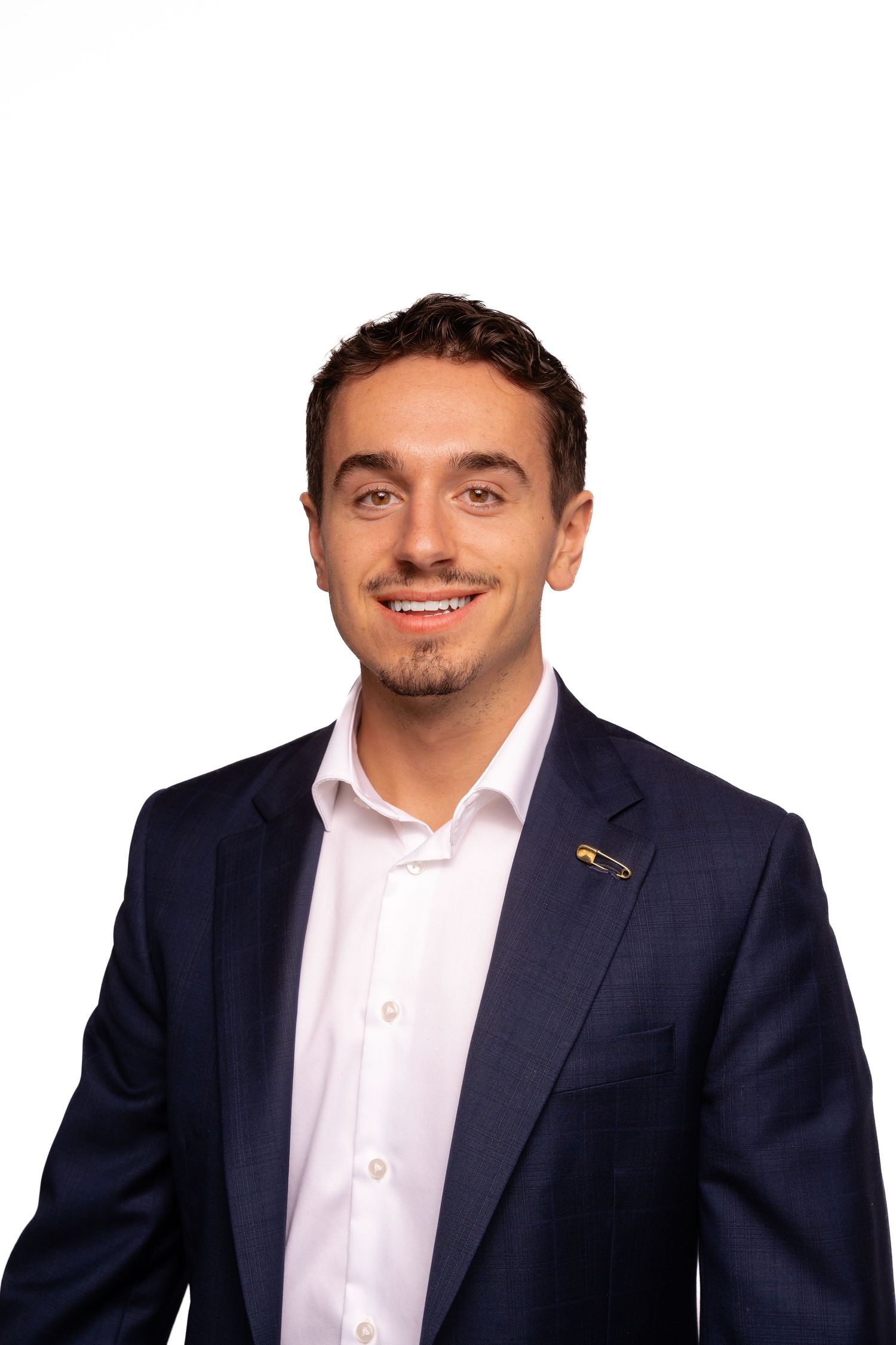 Professional headshot of person in navy suit and white shirt with lapel pin.