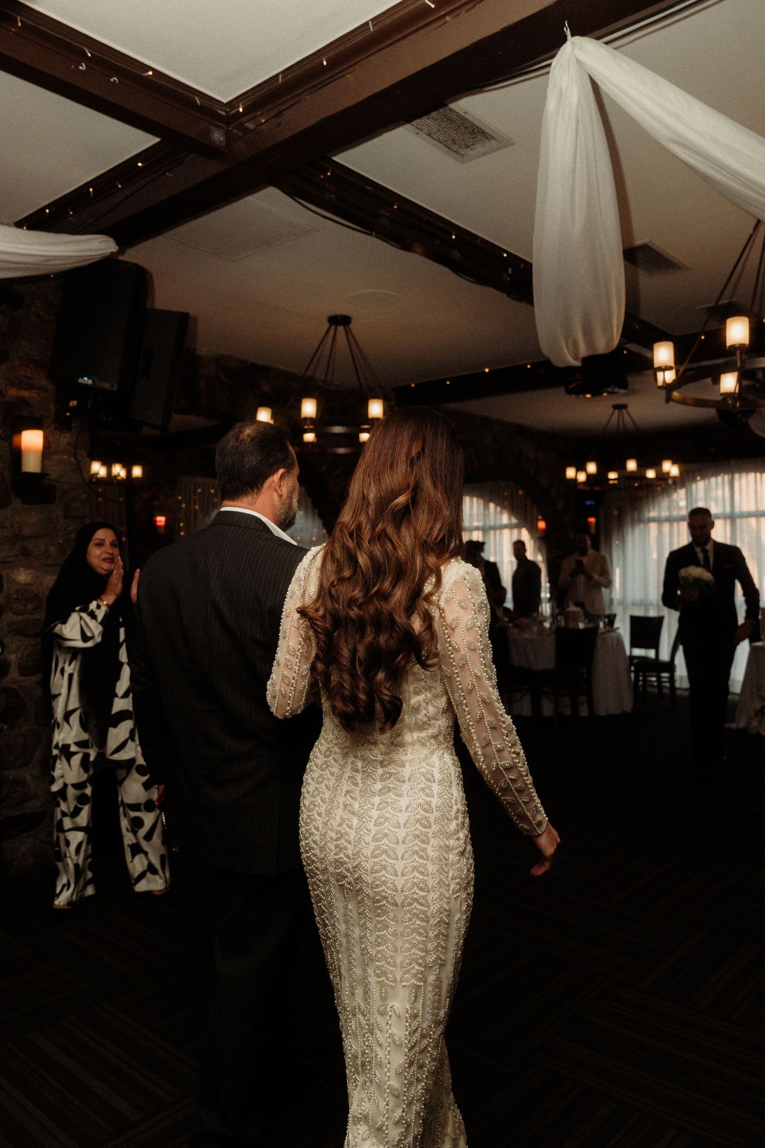 Couple dancing at a wedding reception with warm lighting and exposed wooden beams overhead.