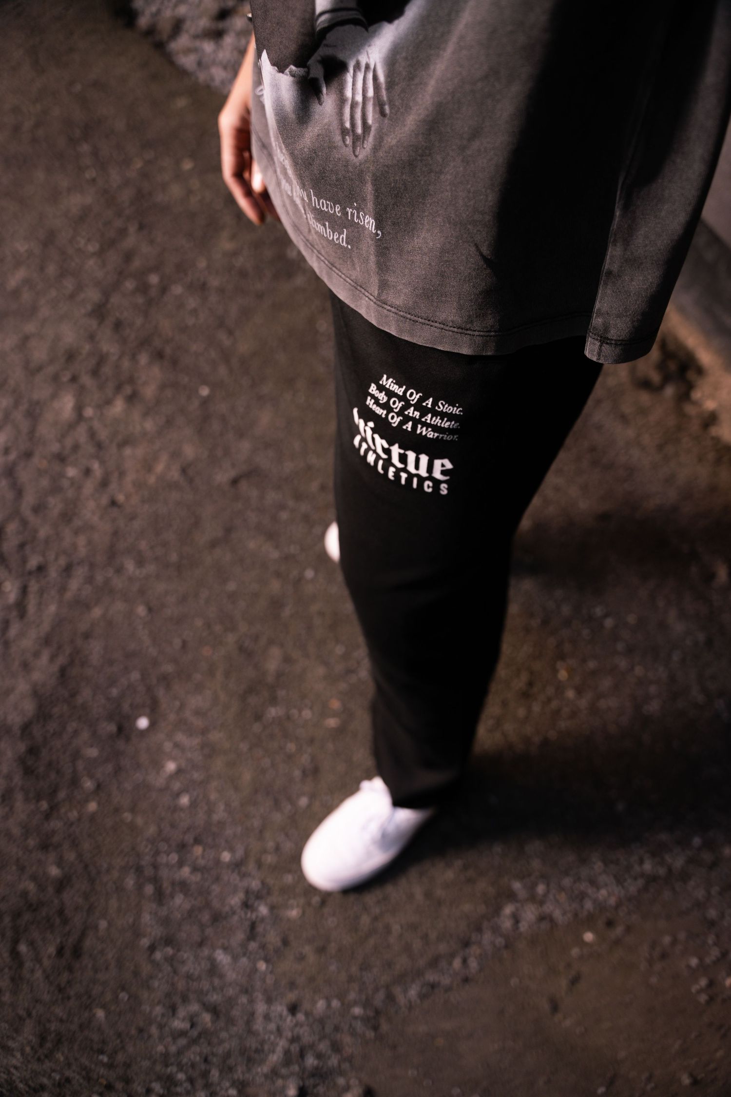 Close-up of black sweatpants with white text detail and white sneakers.