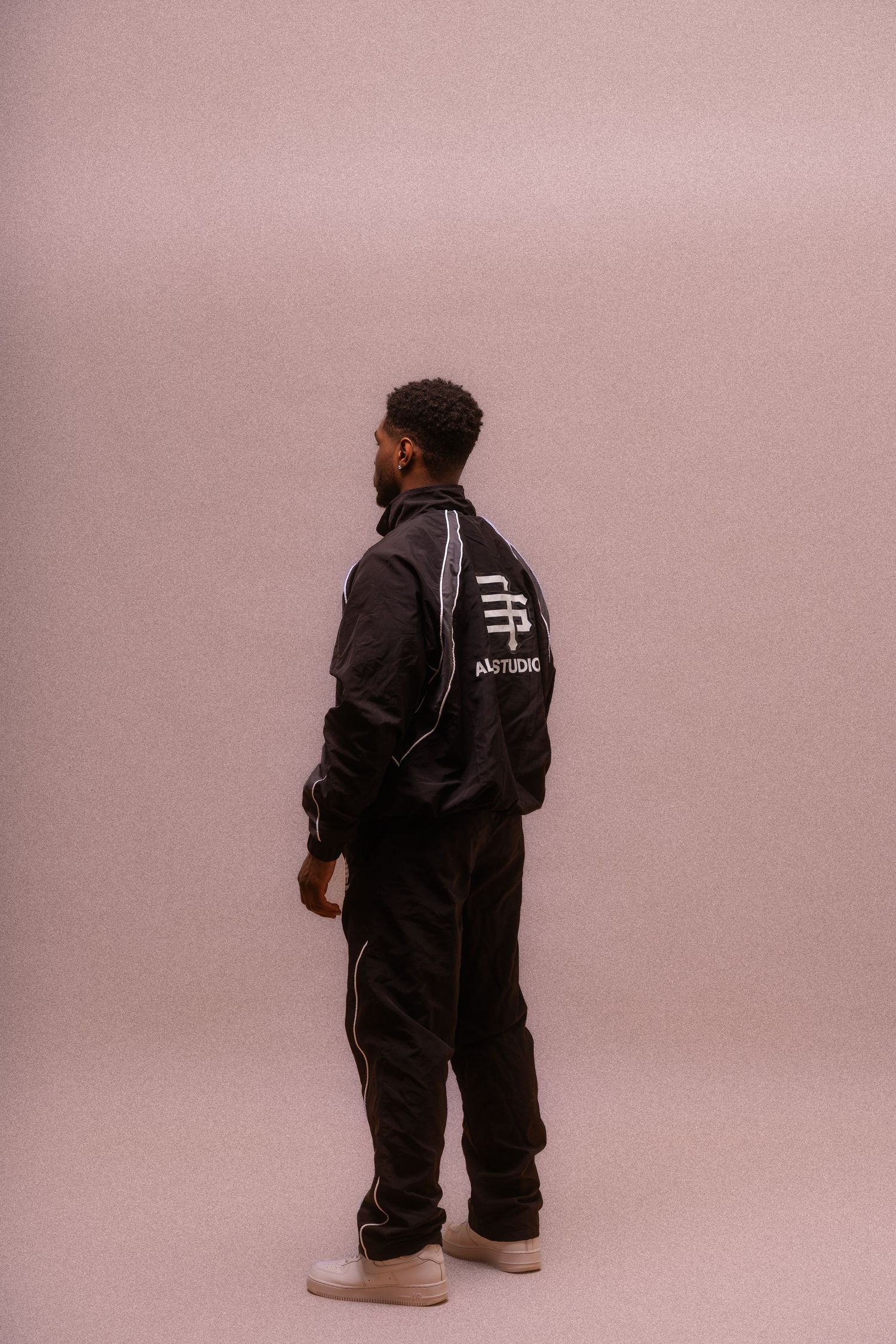 Multiple people wearing black tracksuits photographed from behind on a pink background.