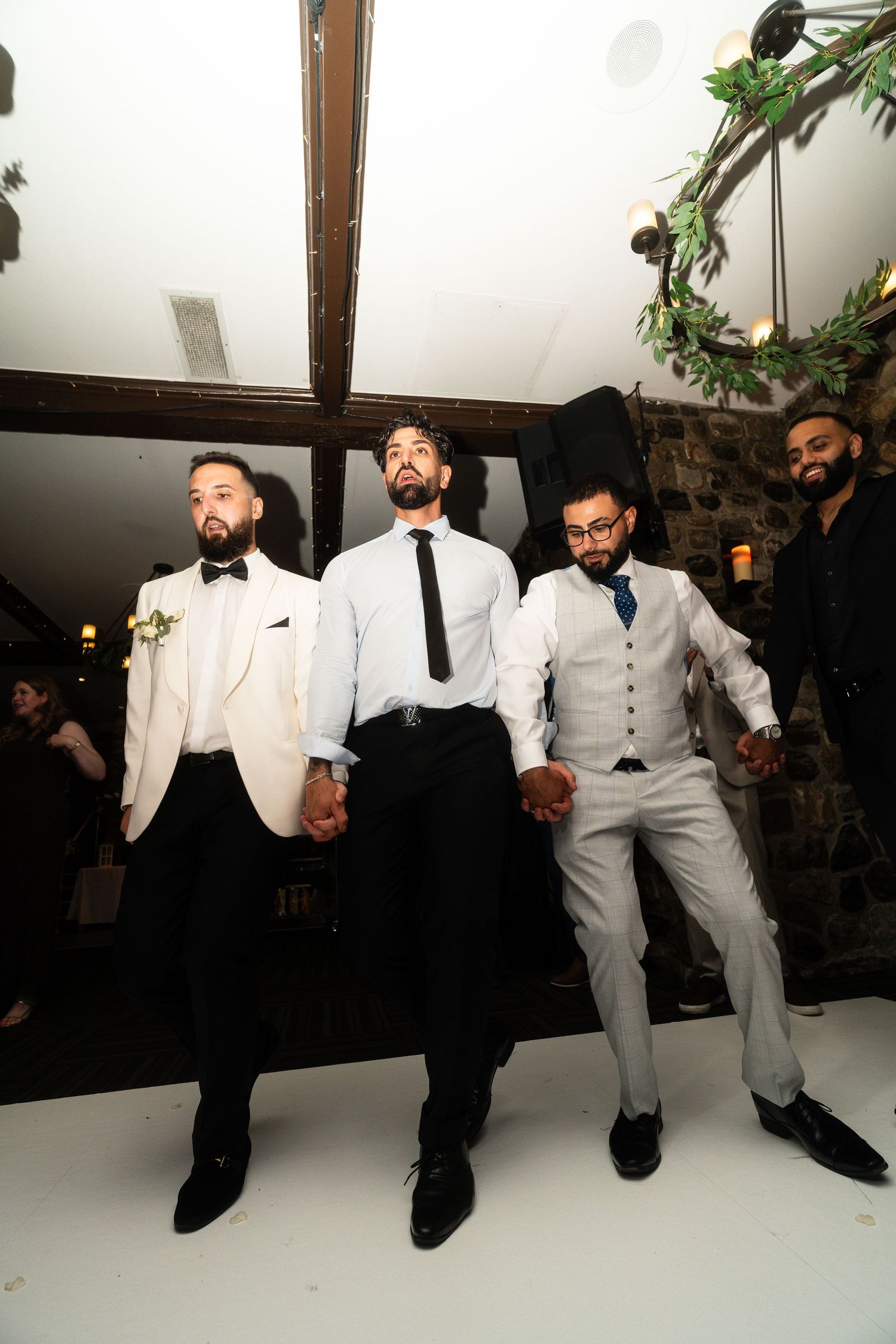A group wearing formal white and black suits sit casually on a white bench in a modern interior space.