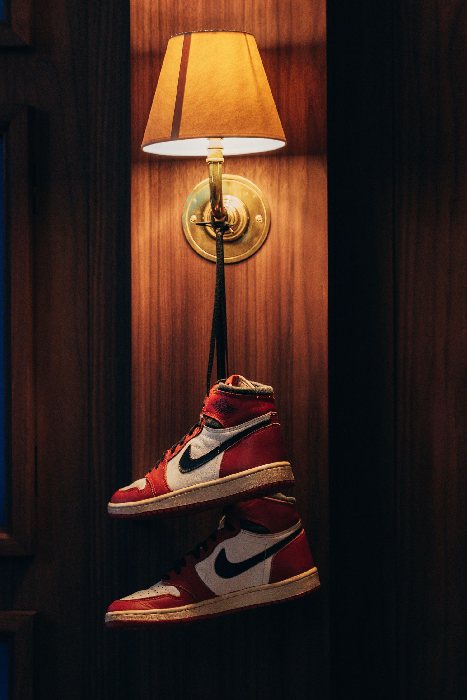 Red and white Nike Air Jordan sneakers displayed under warm lamp lighting against wood paneling.