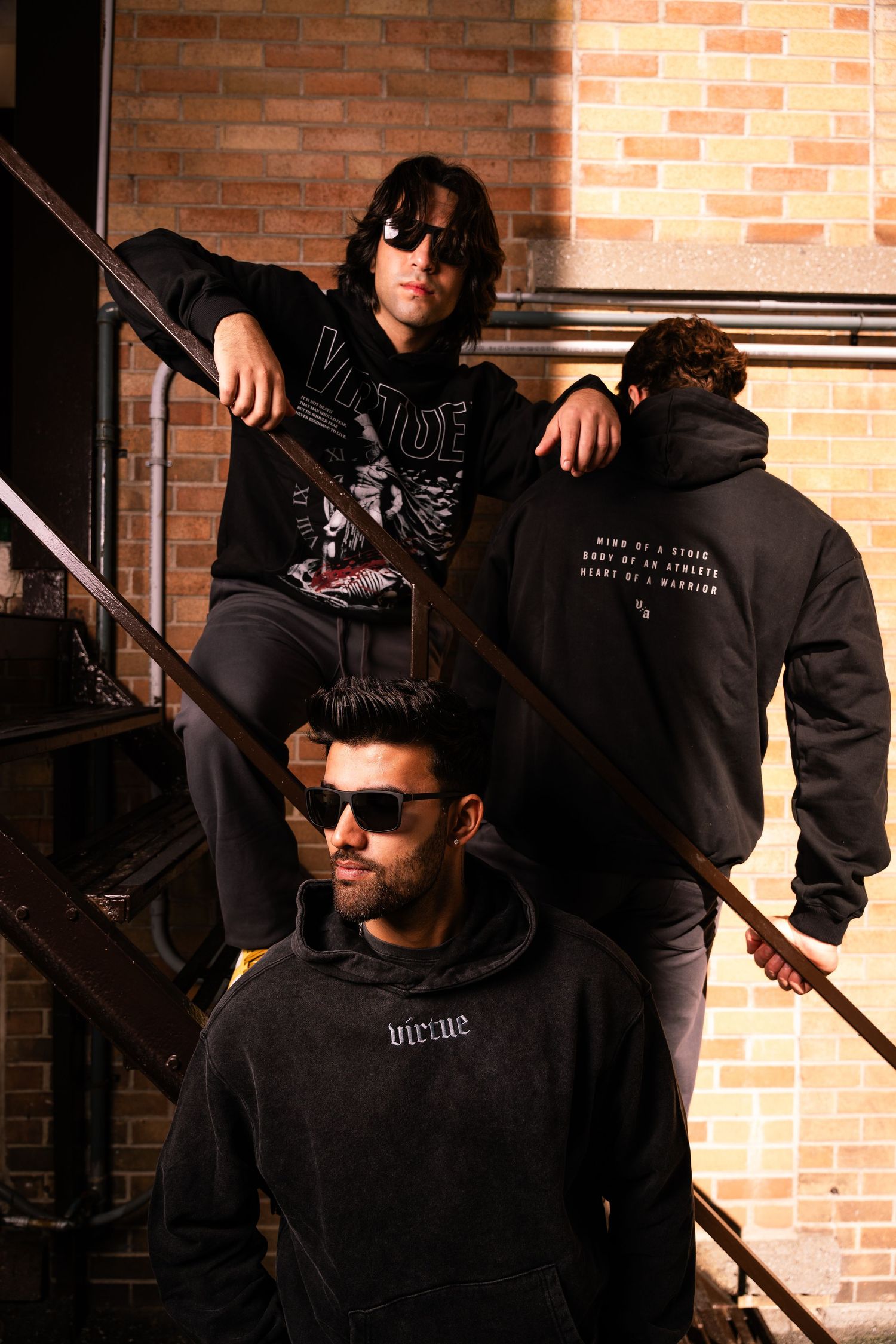 Fashion photo series featuring models in black hoodies against brick wall.