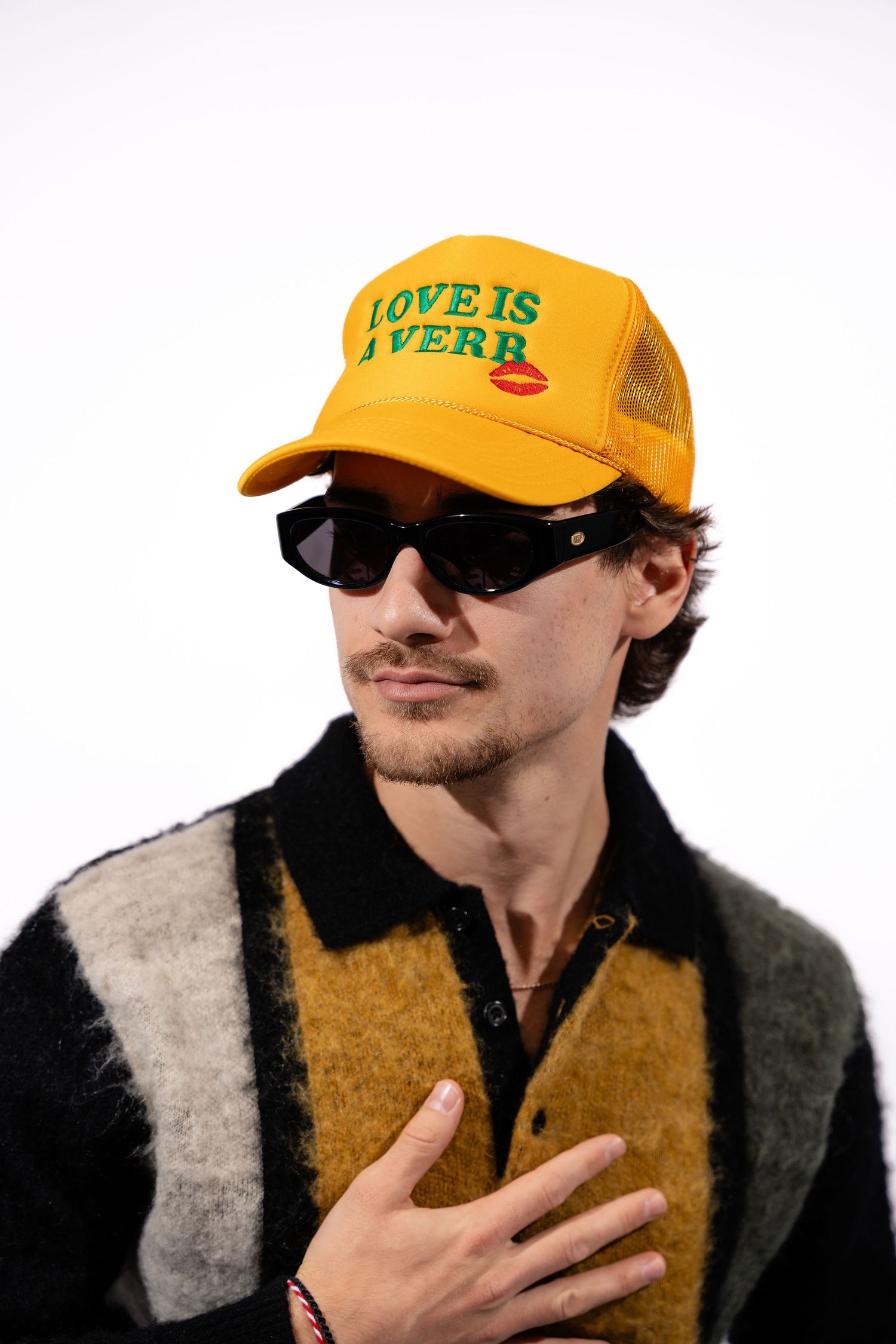 Person wearing yellow cap with 'LOVE IS' text posing against white background.