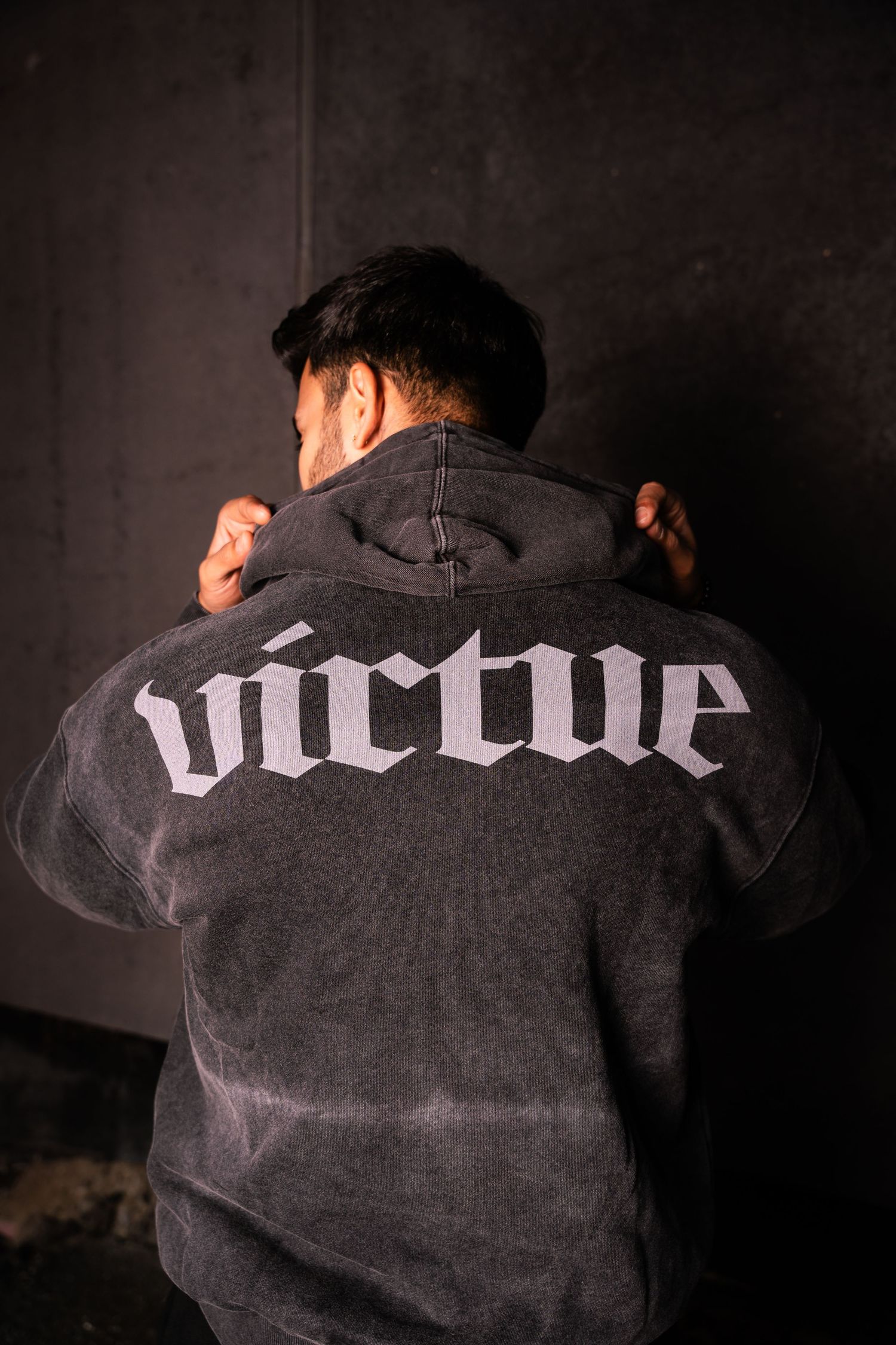 Back view of a black hoodie showing 'virtue' text across shoulders in white gothic font.