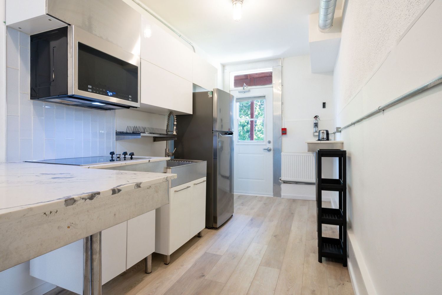 Long white modern kitchen with stainless steel appliances and minimalist cabinetry.