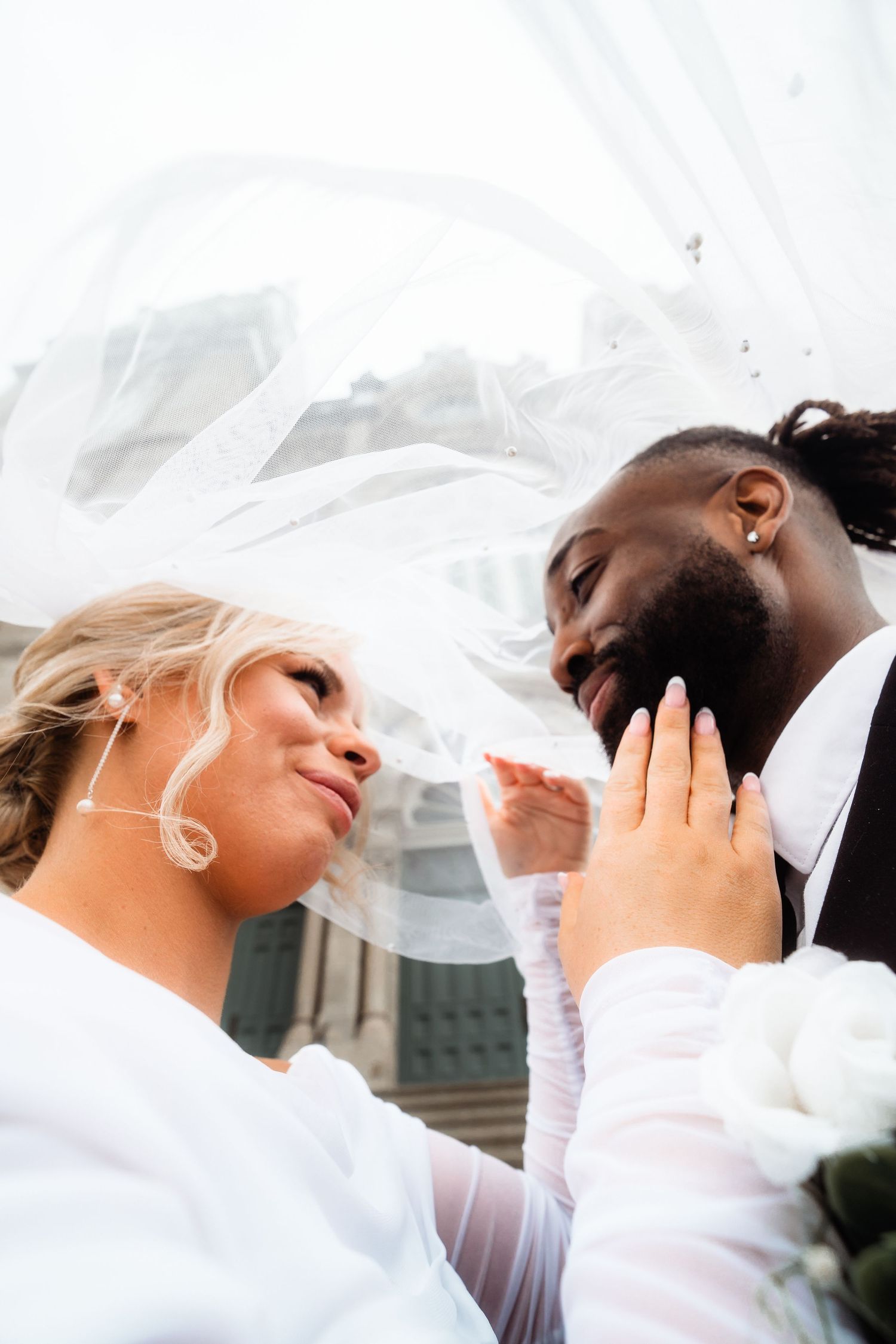 Romantic wedding portraits with flowing white veil against architectural backdrop.