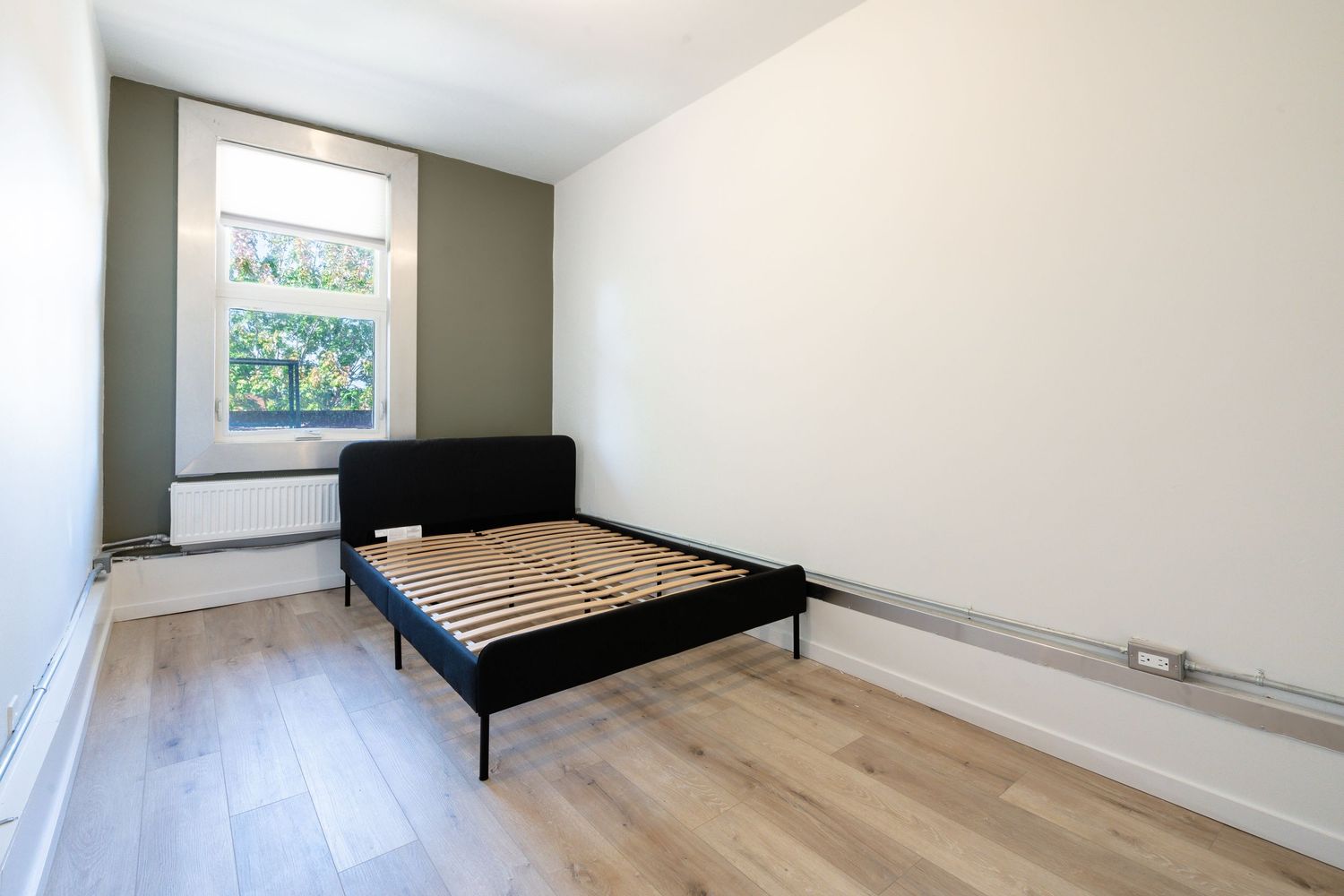 Empty bedroom with light hardwood flooring and black metal bed frame.