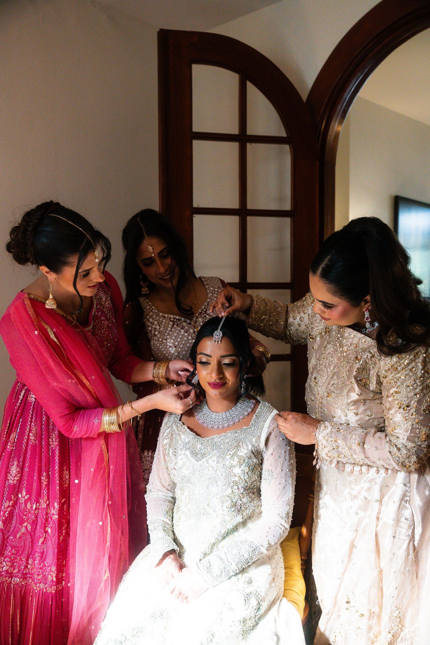 A group wearing elegant traditional outfits in white and pink gather together in an indoor setting.