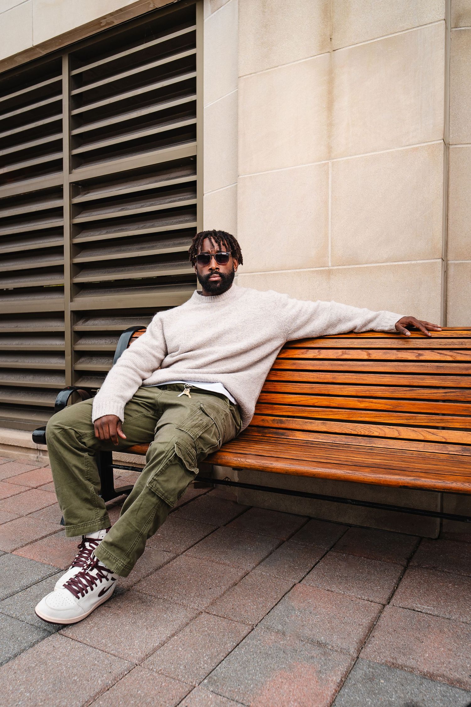 Person in white sweater relaxing on wooden bench against building exterior.